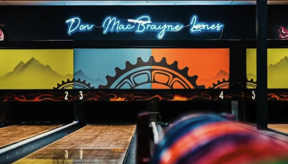 Colorful bowling ball in motion beside polished lanes at The Werks Colorado, with numbered lanes and a vibrant mural visible in the background