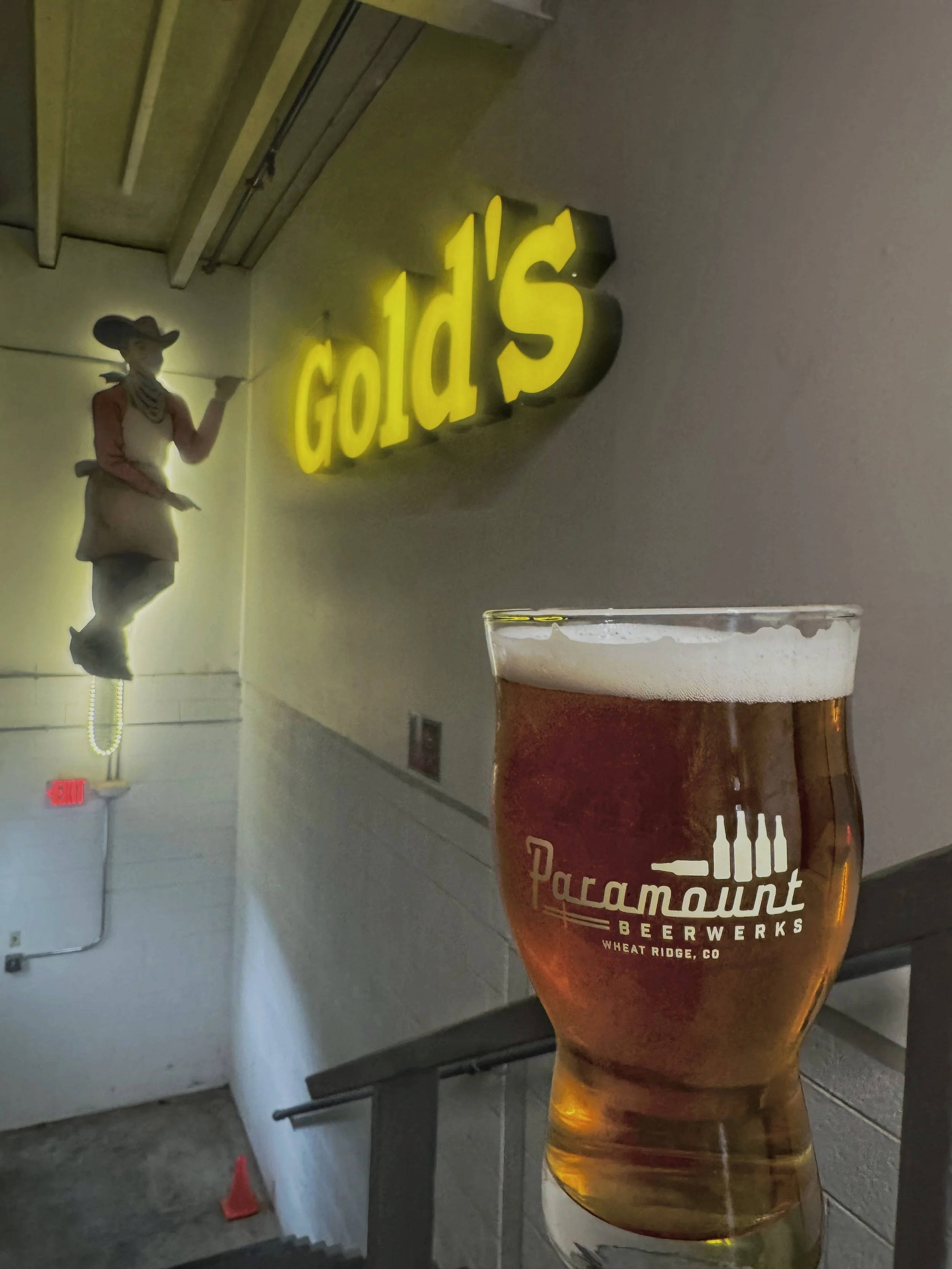 Pint of amber Gold’s Lager in a Paramount BeerWerks glass beneath the illuminated Gold’s sign.