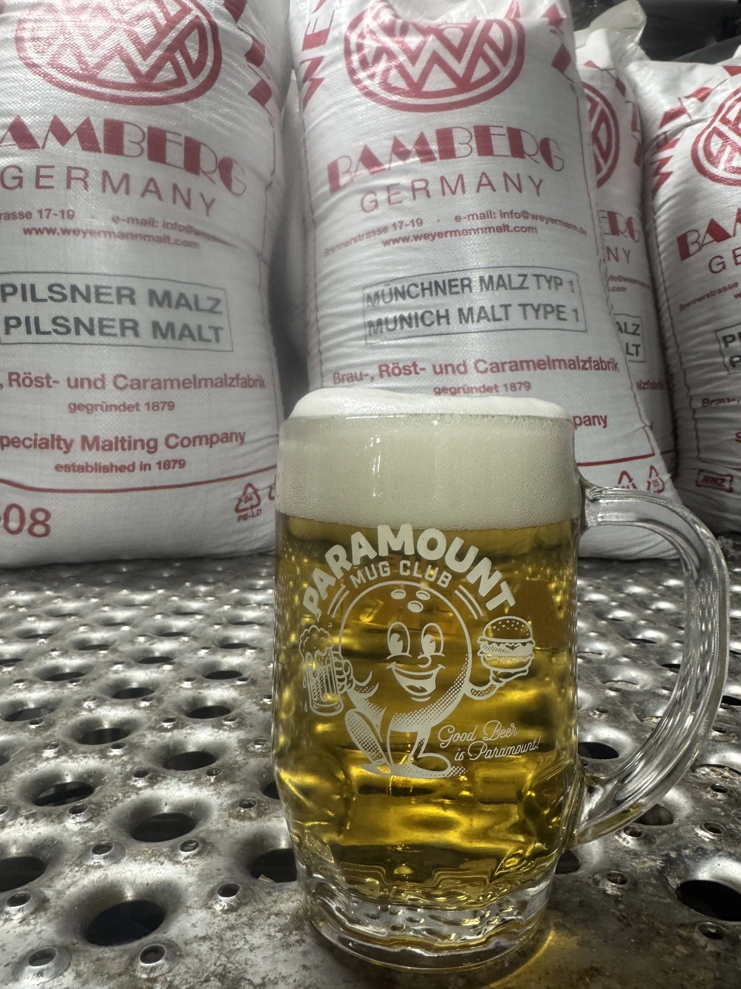 Paramount Mug Club stein filled with golden Premium Lager in front of Weyermann malt bags.