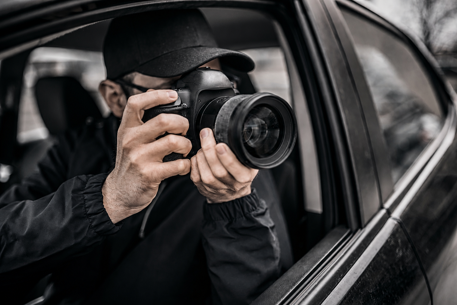 Investigator photographing a subject from inside a vehicle during surveillance.