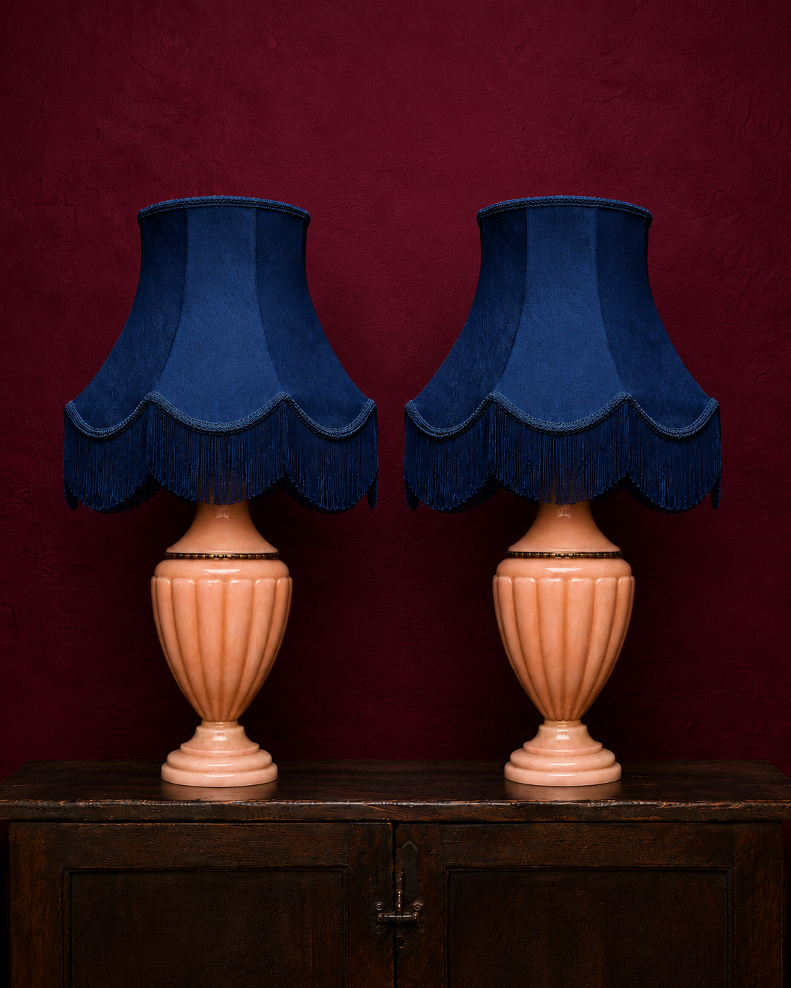 Refined pair of table lamps with softly fluted pink alabaster bases and deep blue fabric shades, finished with scalloped edges and generous fringe. The delicate tones of the stone contrast beautifully with the rich fabric, while the classical form gi