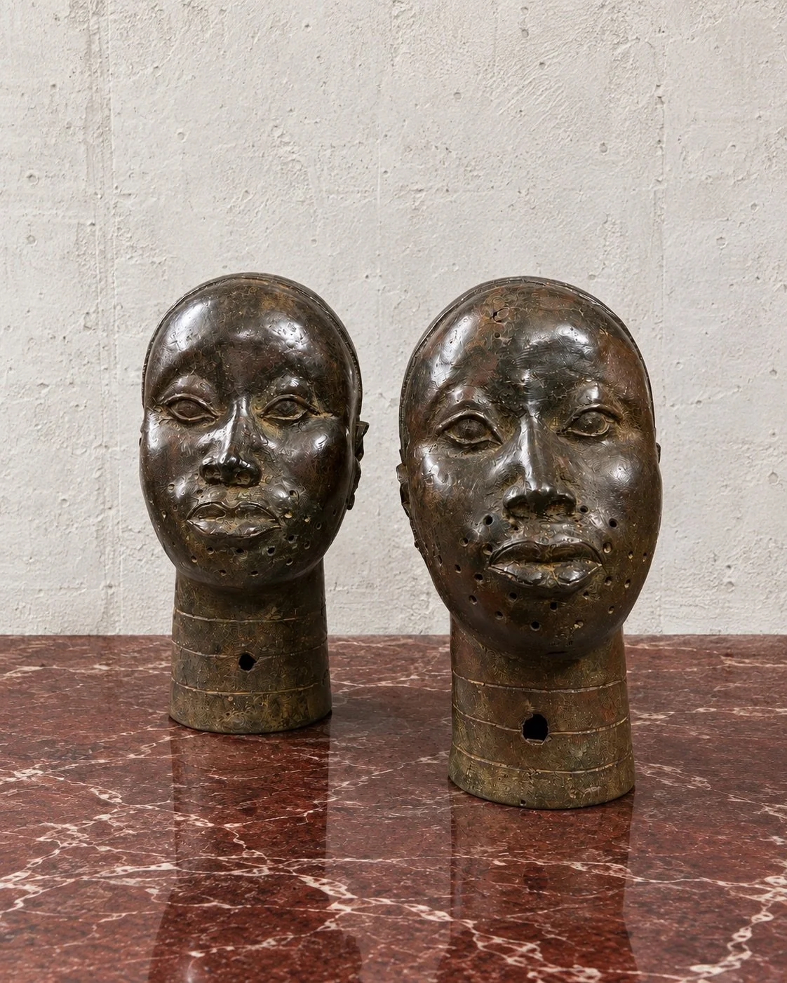 Refined pair of cast African heads, attributed to Cameroon, distinguished by expressive features, perforated detailing and a richly aged patina. Subtle irregularities across the surfaces enhance their tactile quality, giving the works a compelling pr