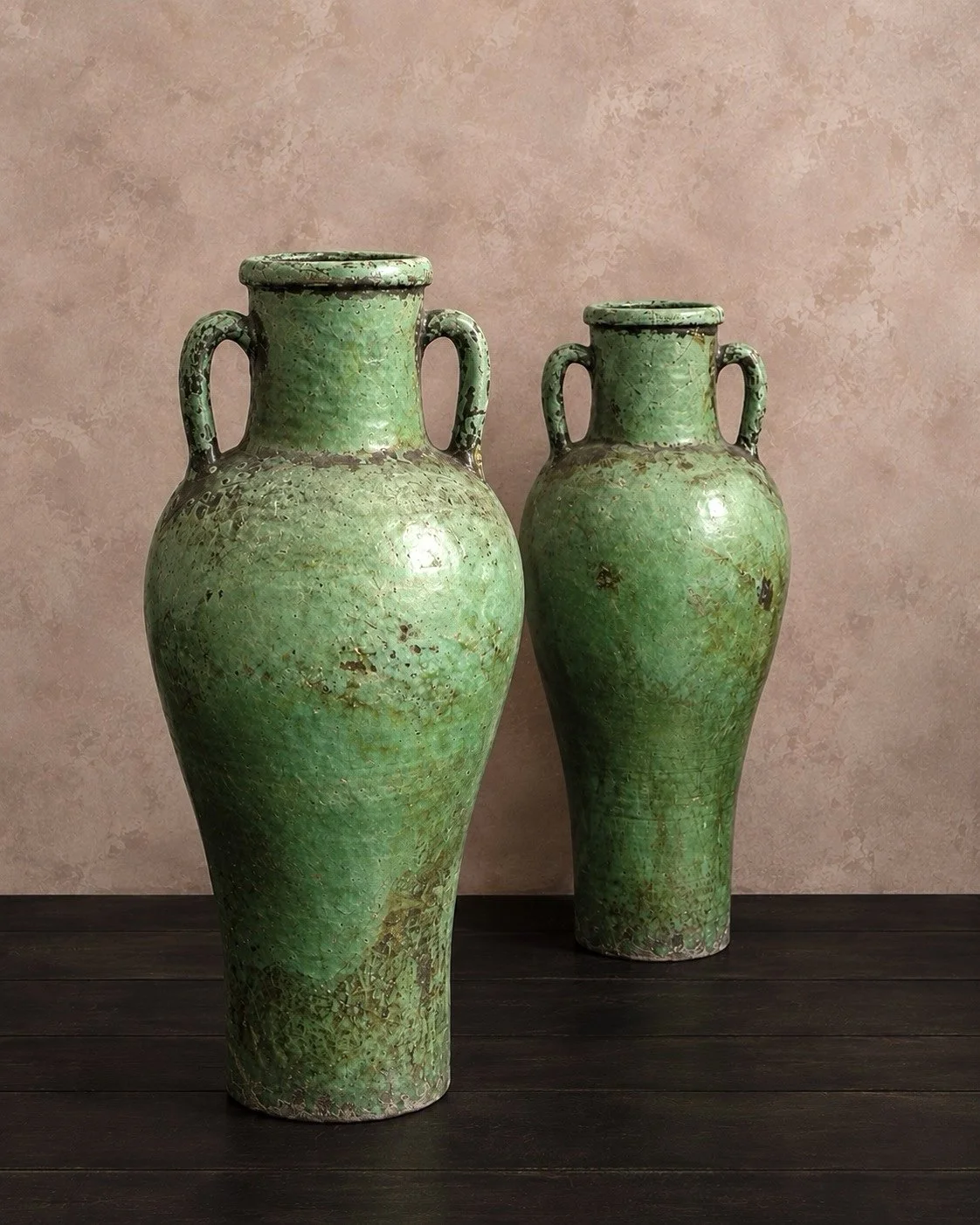 Characterful pair of ceramic vessels with generous, elongated proportions and distinctive twin handles. Their varied green glaze reveals subtle shifts in tone and texture, while areas of natural wear lend depth and visual interest. The irregular fini