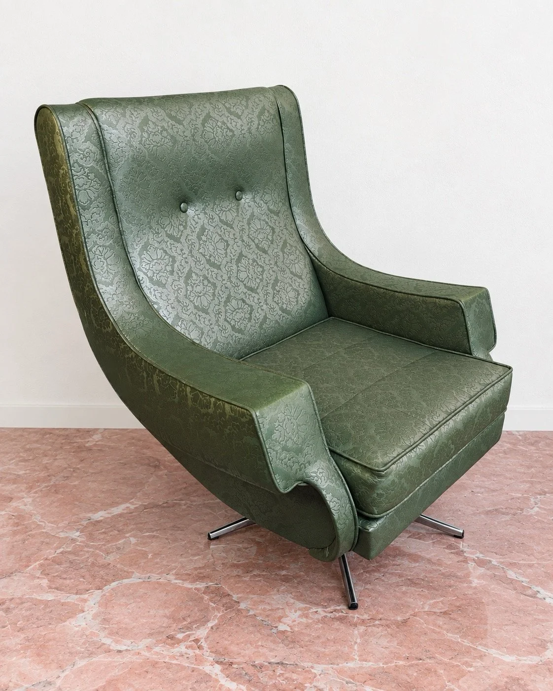 Dating from the mid-century era, this vintage swivel chair combines a sculptural silhouette with an elegant, enveloping form. Richly patterned green faux-leather upholstery covers the high, gently curved back, softly flared arms and deep seat, while 