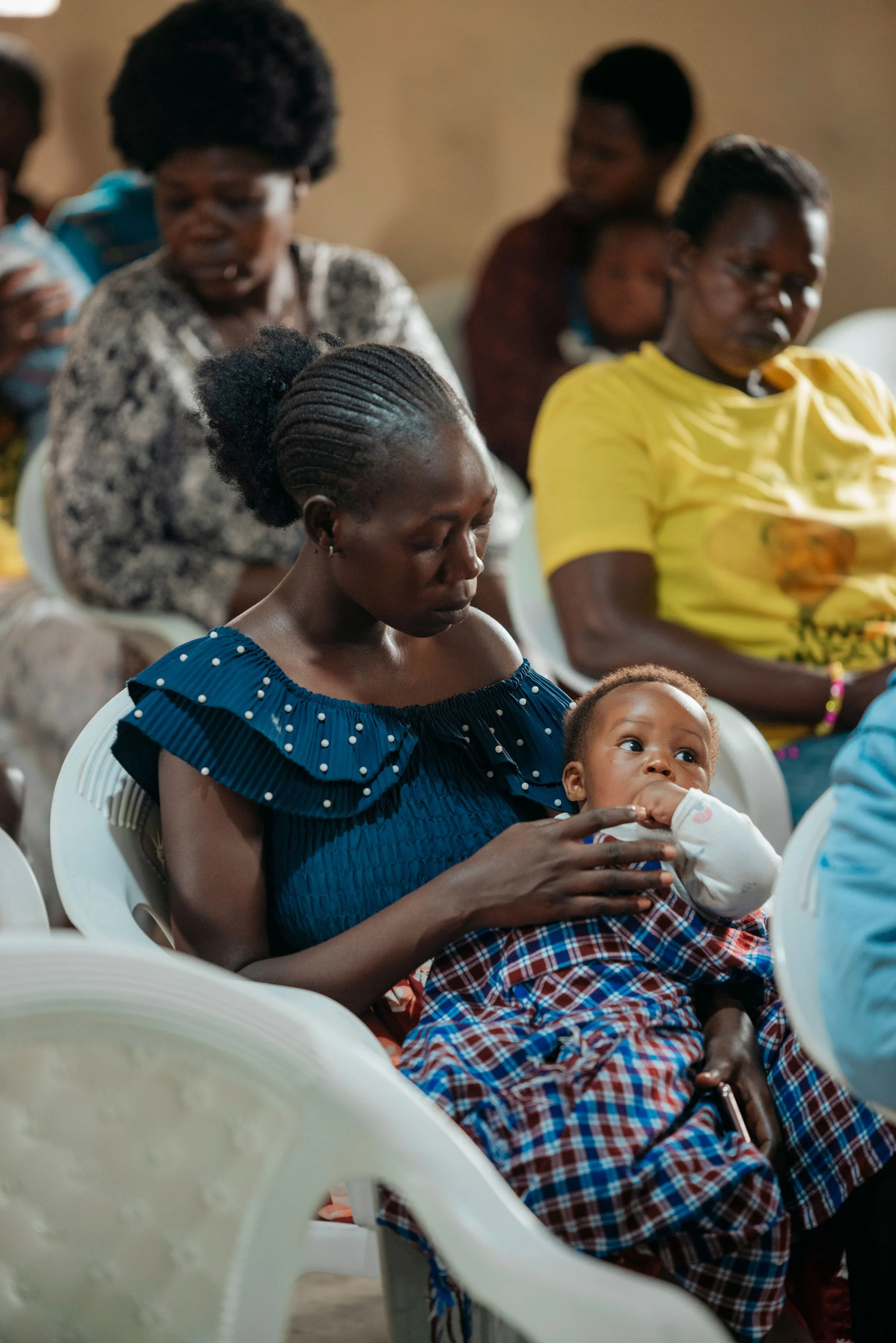 A group of women and a child sitting on white plastic chairs, with the women holding the child in their laps.