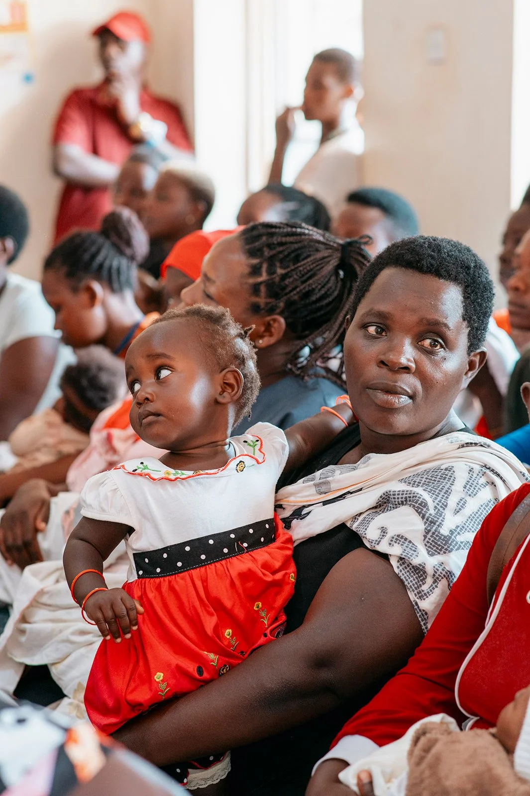 A woman holding a young child in a crowded room during an event or gathering.