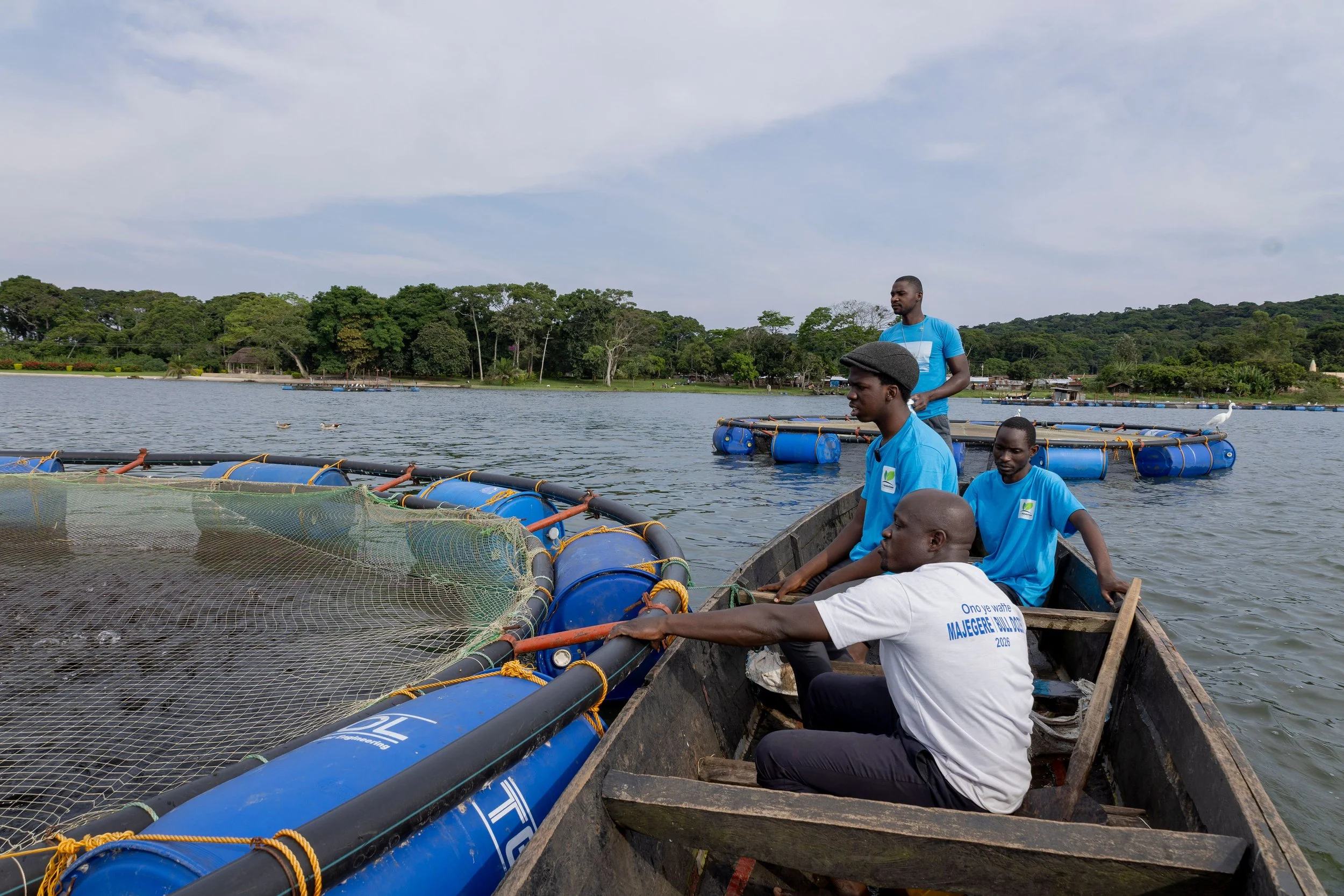 A group of men in a boat on a body of water with green trees along the shoreline and a partly cloudy sky overhead.
