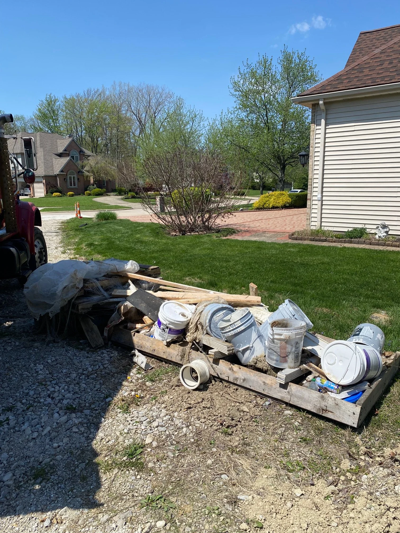 Heap of construction debris including white buckets, wood planks, and plastic sheeting in a yard with green grass and houses in the background. h&h property services in Strongsville Ohio