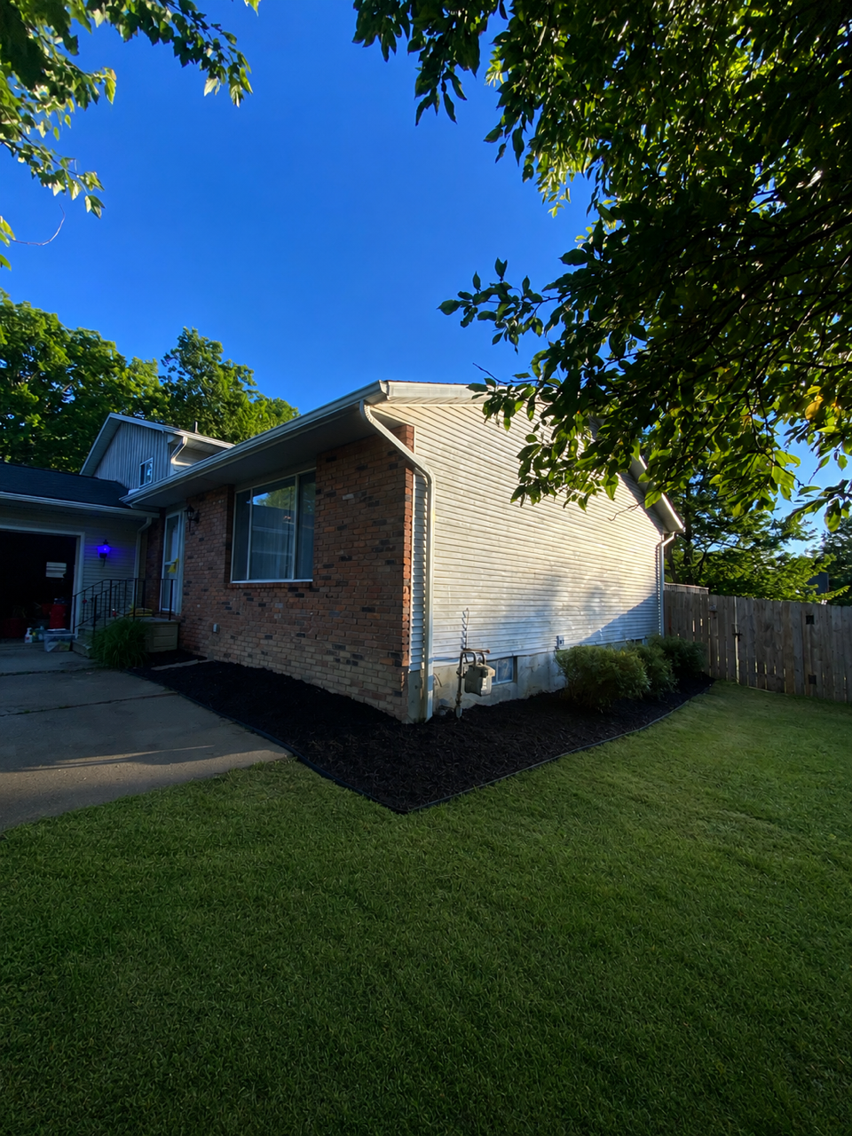 A suburban house with a brick and siding exterior, a gable roof, a front window, and a small landscaped yard with grass and mulch.