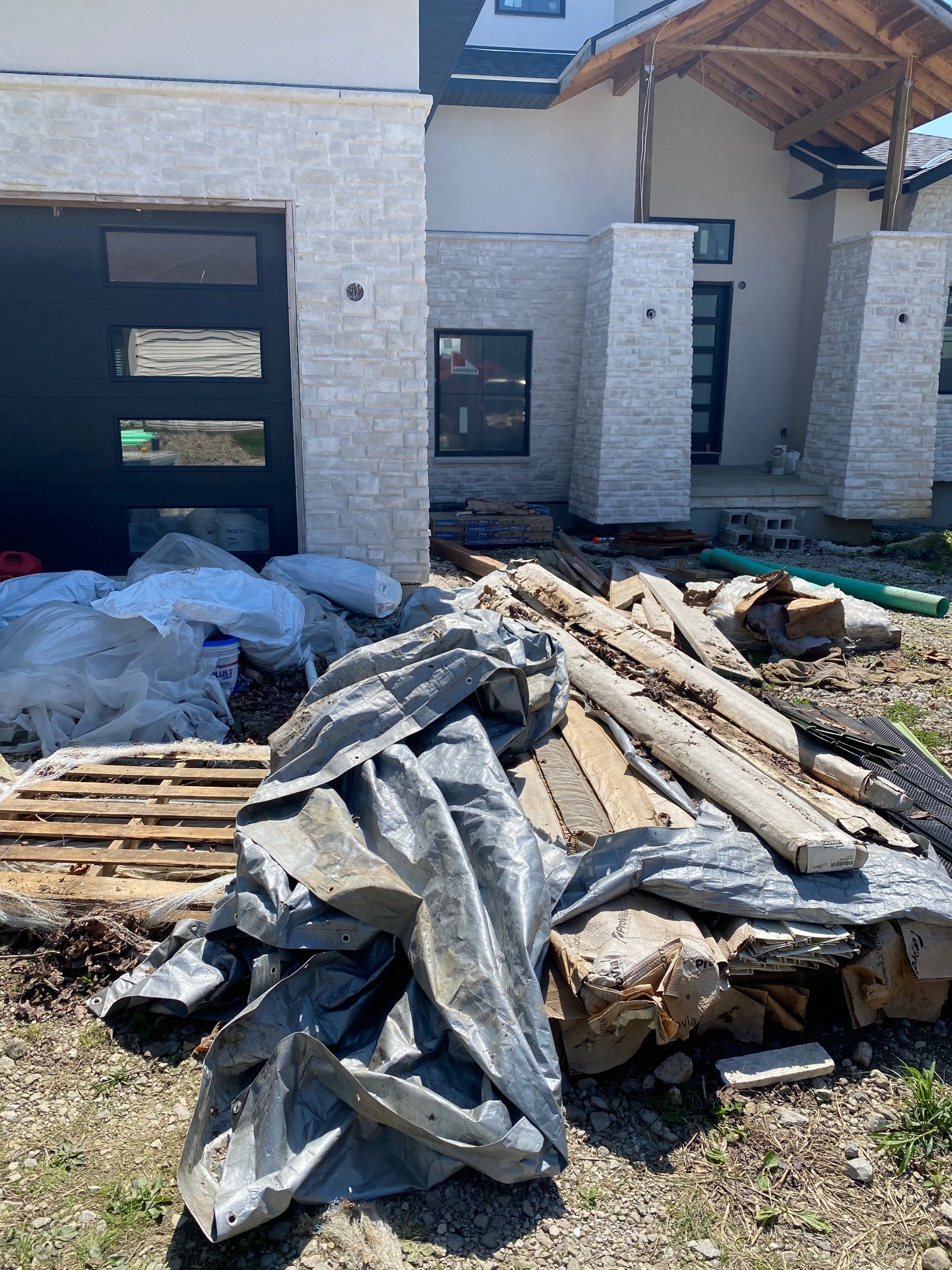 Construction site with debris, wood, and building materials in front of a partially built house with stone and stucco walls.  h&h property services in Strongsville Ohio
