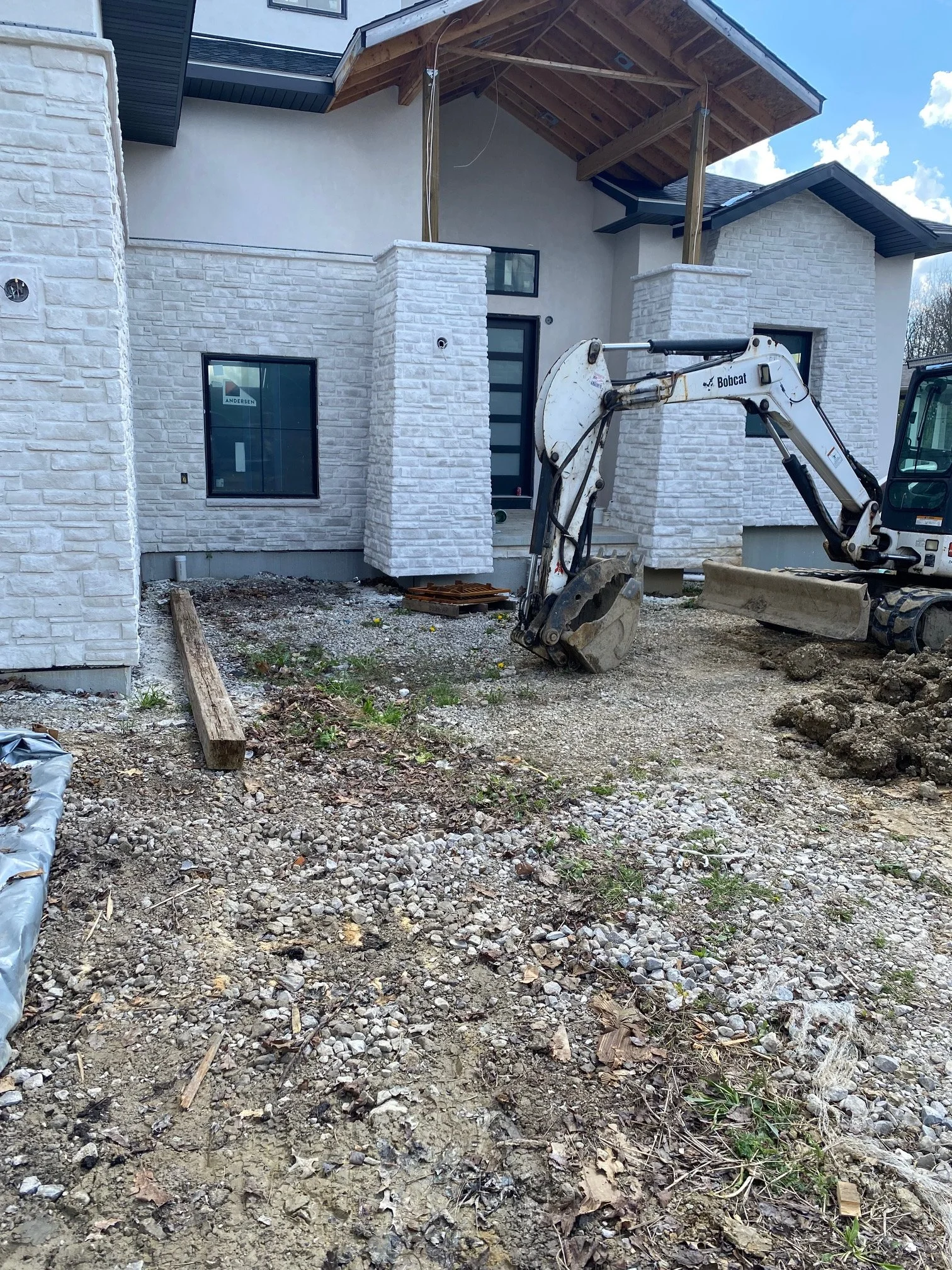 Construction site in front of a house with white brick exterior, on-going work with a small excavator and building materials scattered around. Strongsville Ohio