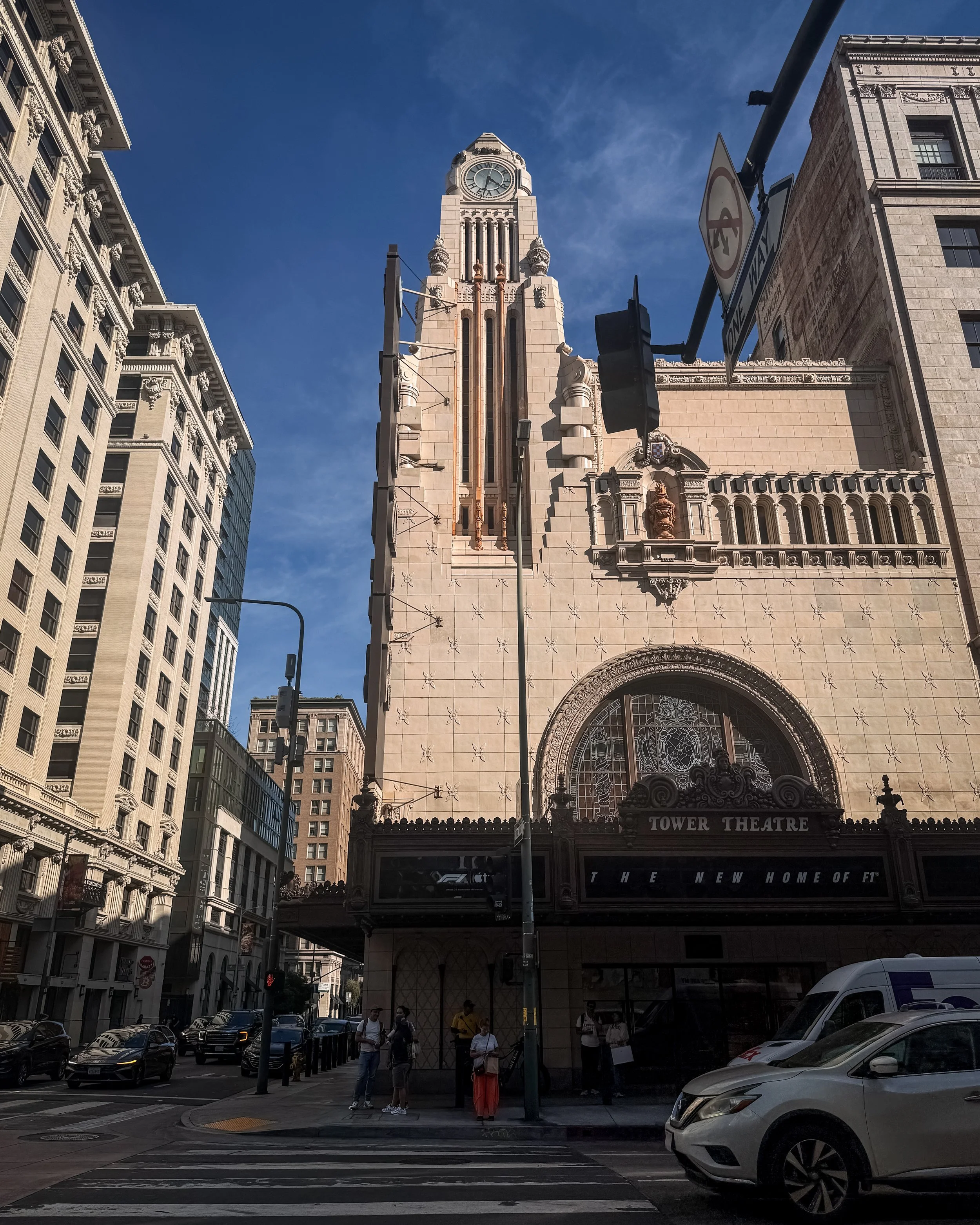 Street facade view of the historic Tower Theatre building in Downton Los Angeles, California, USA, now an Apple Store, with people walking on the sidewalk and cars parked along the street. 