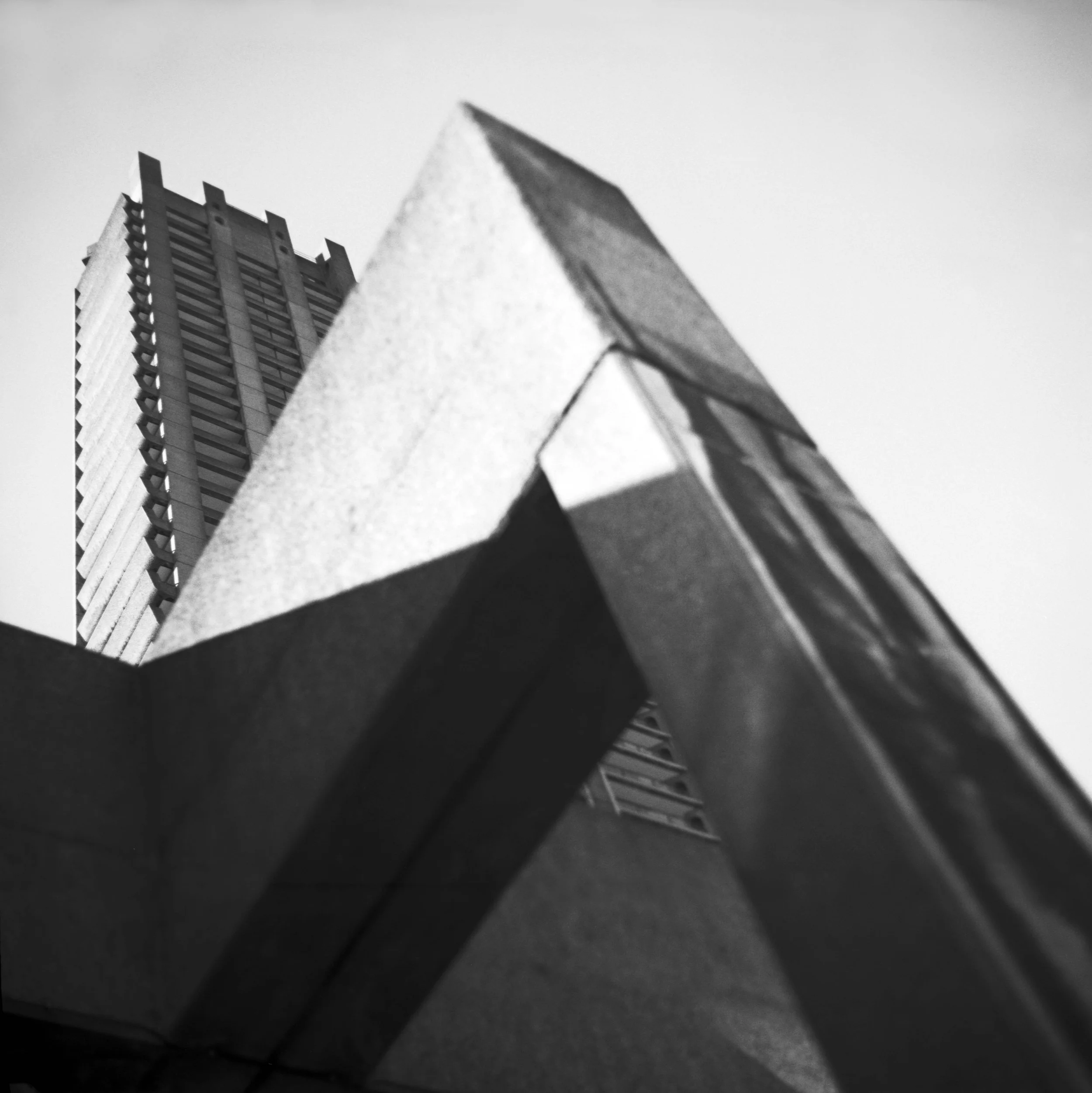 Low-angle black-and-white photo of brutalist skyscrapers in London, United Kingdom, viewed from below against a clear sky. Architecture photograph.