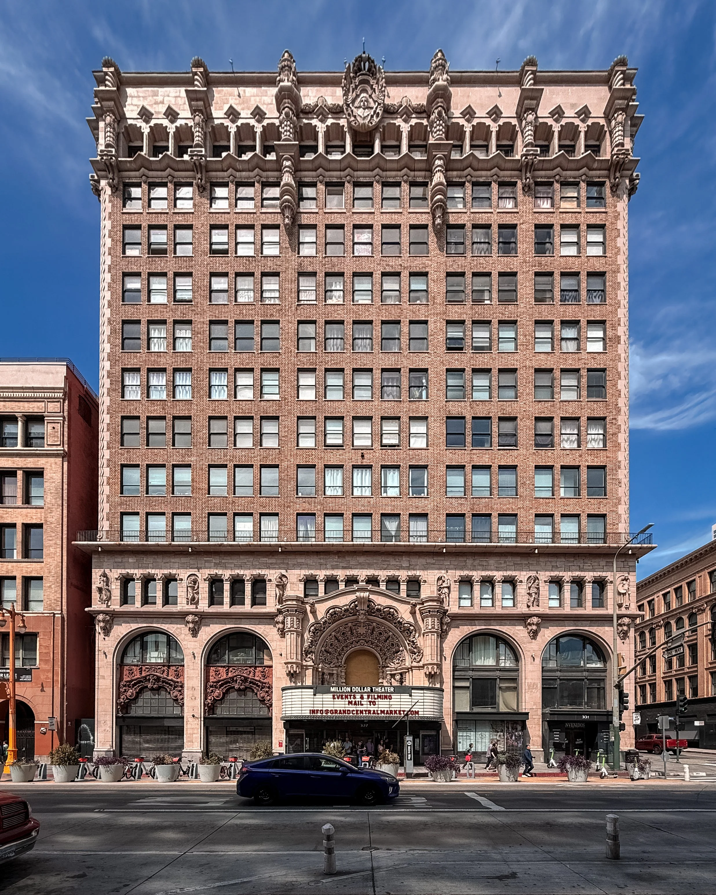 A street scene in Downton Los Angeles in California, USA. The building has a decorative facade with intricate stone carvings, large arched entrance doors, and numerous windows. 