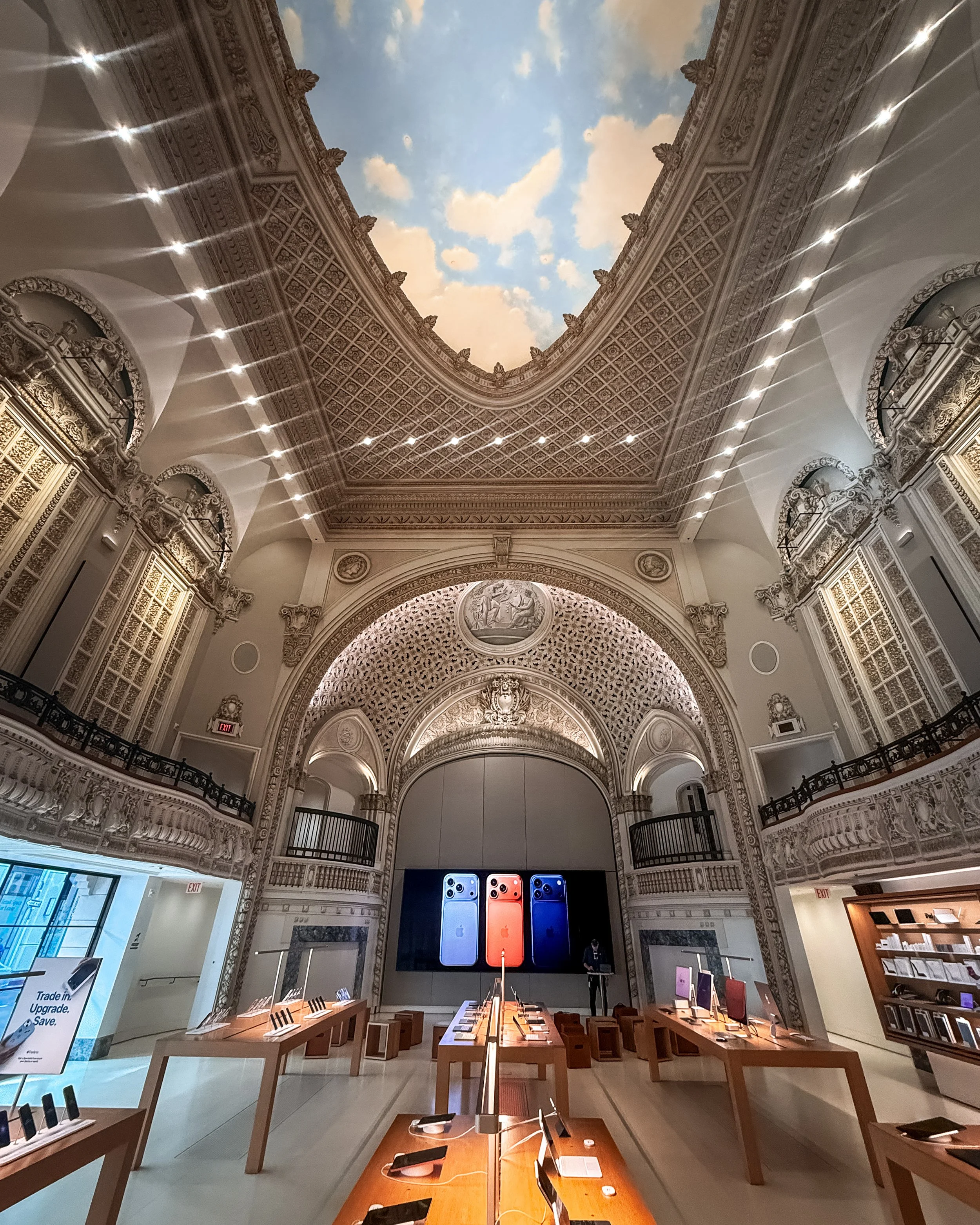 Interior of an Apple Store in Downton Los Angeles, California, USA, in the former Tower Theatre. High ornate ceiling, classical architecture, and a sky mural ceiling. Several tables with iPads and Apple products. 
