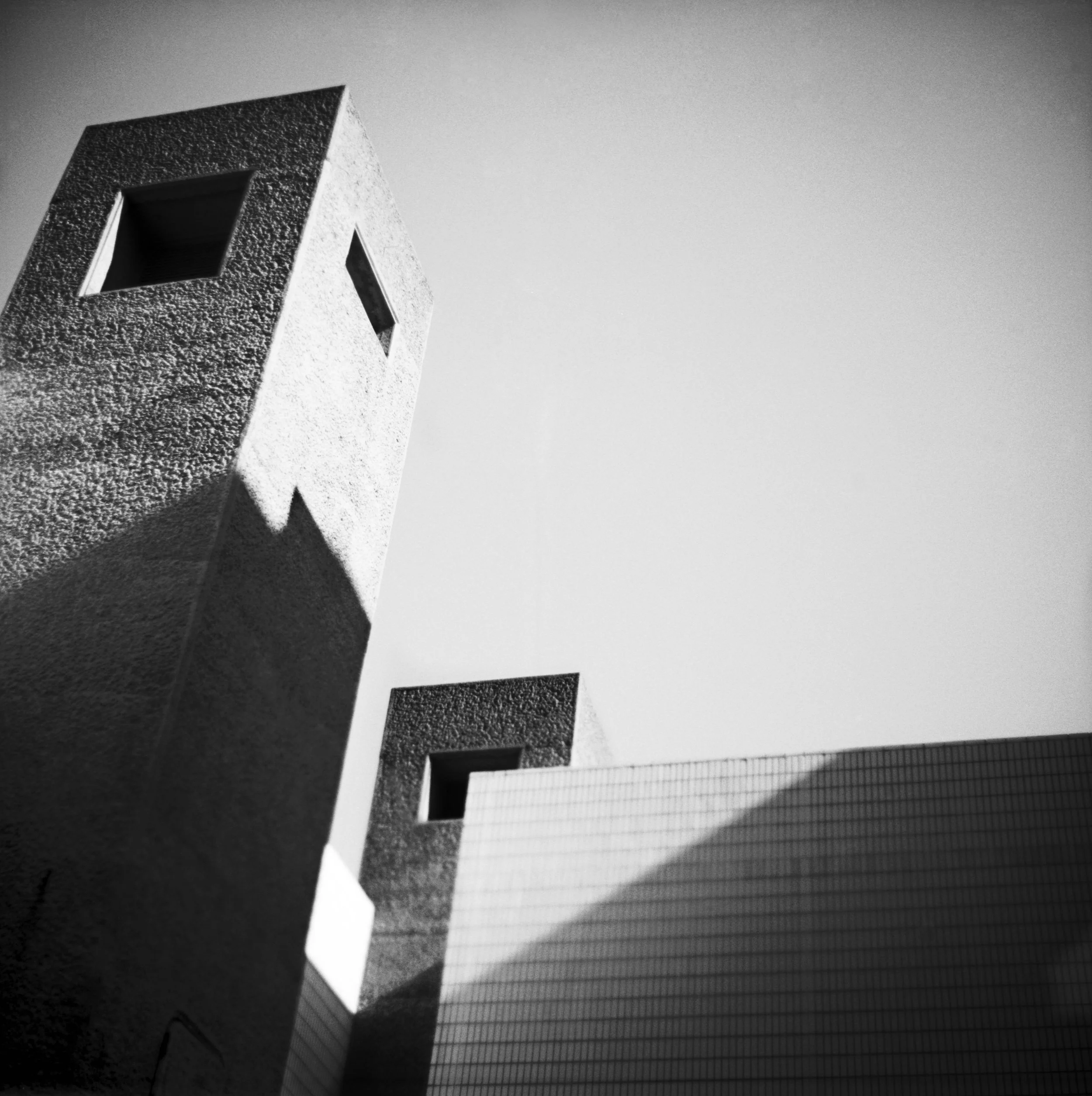 Close-up of a brutalist building's corner with textured concrete exterior, set against a clear sky. Black and white architecture photograph in London, United Kingdom.