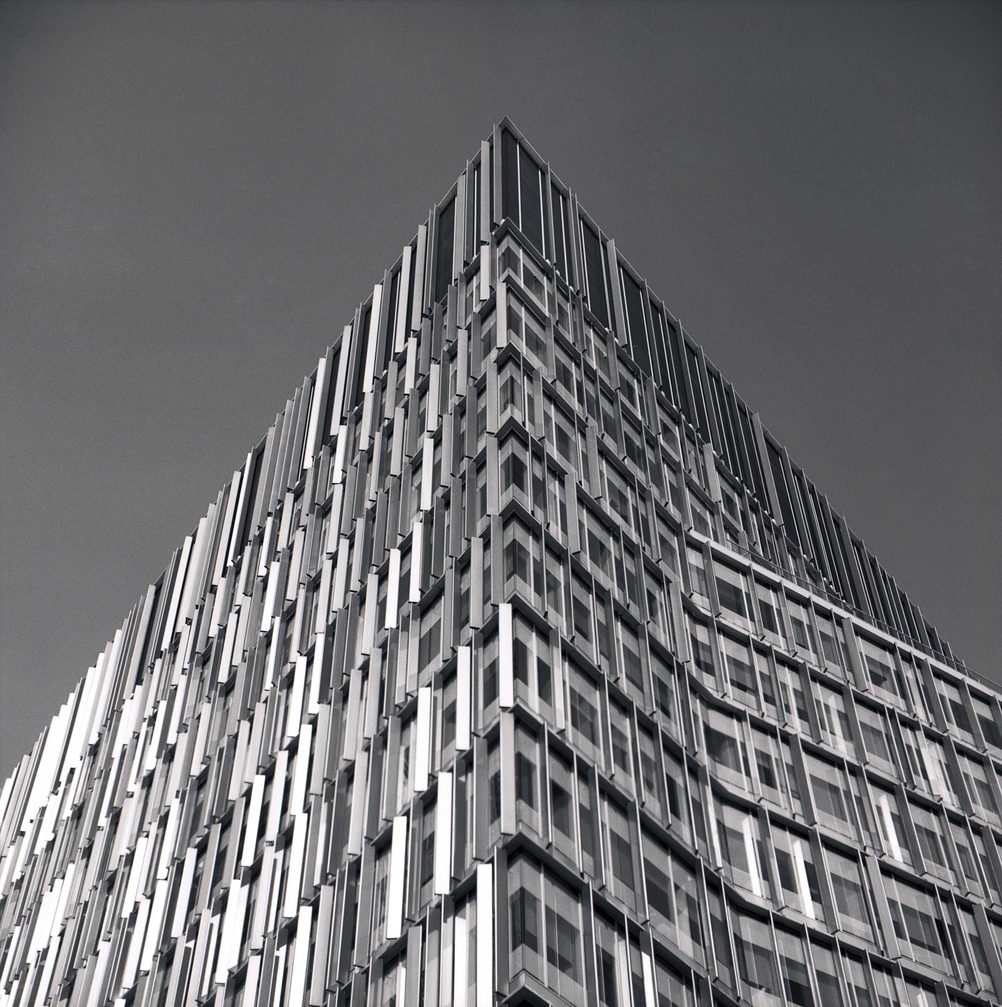 Close-up of a modern, angular building with a glass and metal facade reaching toward sky in London, United Kingdom. Black and white architecture photograph.