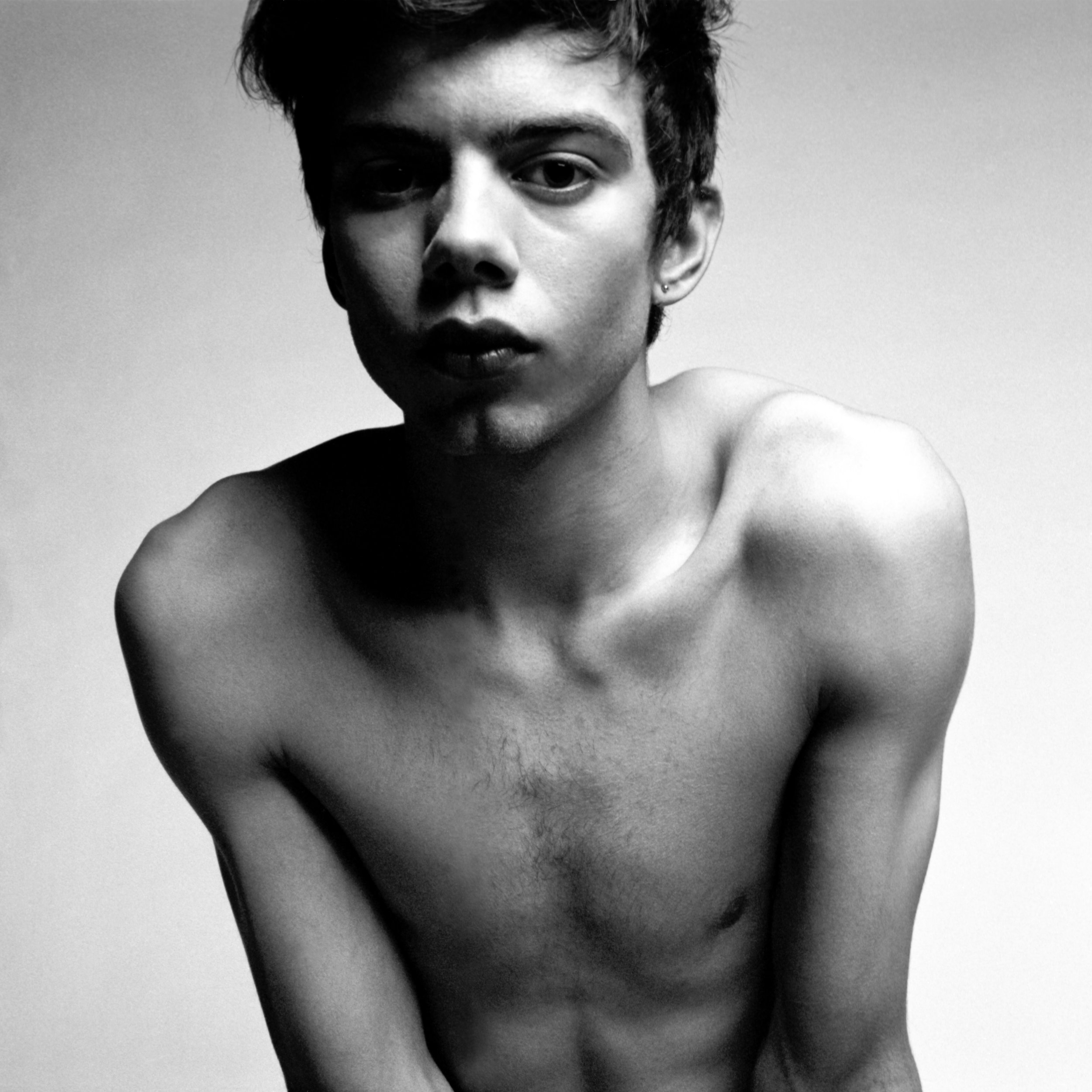 Black and white close-up portrait of a young man with short, messy hair looking directly at the camera, head slightly tilted. Medium format film photograph.
