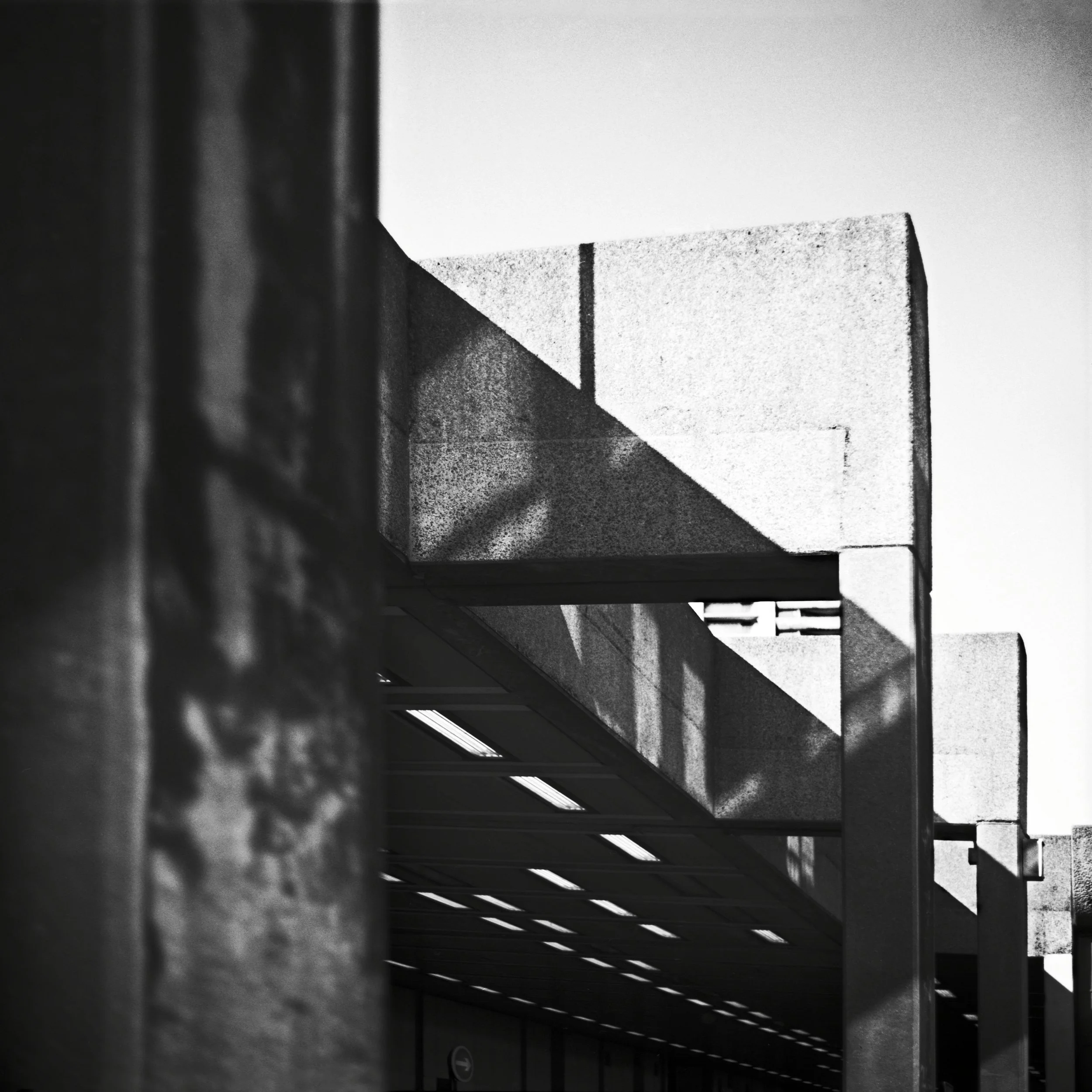 Black and white photo of a Brutalist architectural building with straight lines and geometric shapes, photographed from a low angle in London, United Kingdom. Architecture photograph.