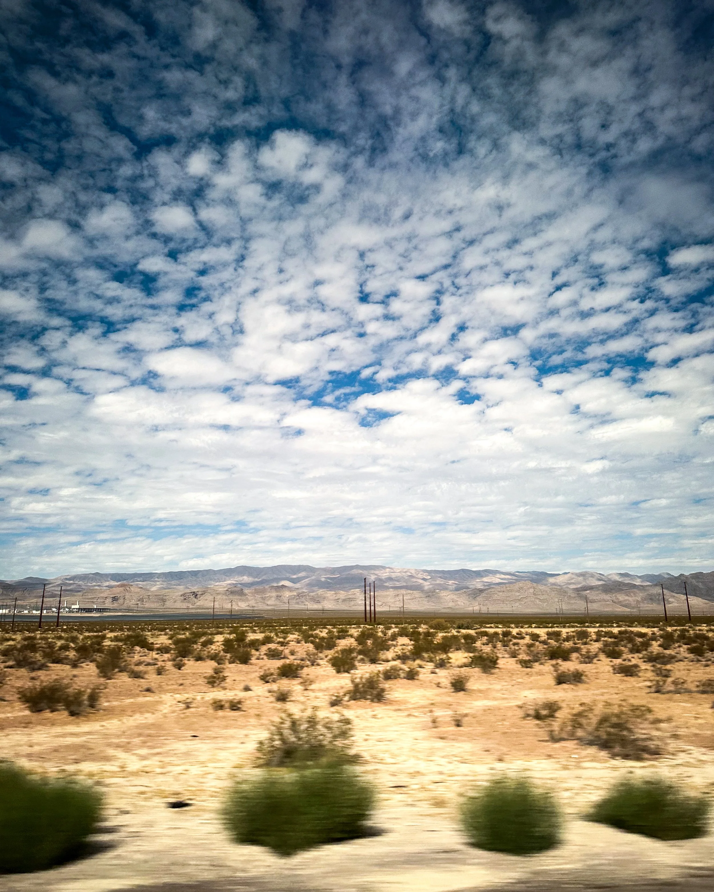Desert landscape with mountain range in the background under a partly cloudy sky.