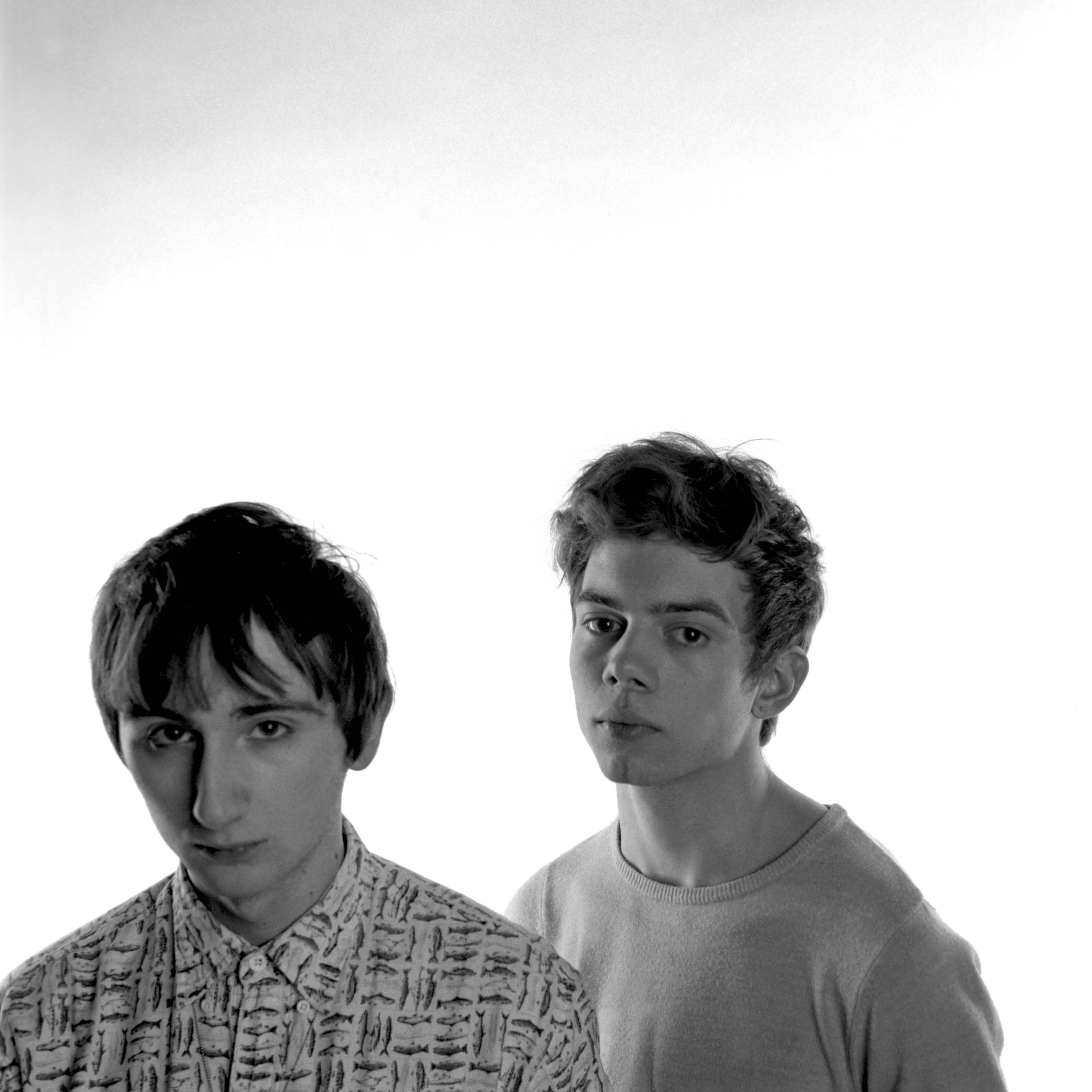 Black-and-white portait photo of two young men standing close together, looking at the camera. Medium format film photograph.