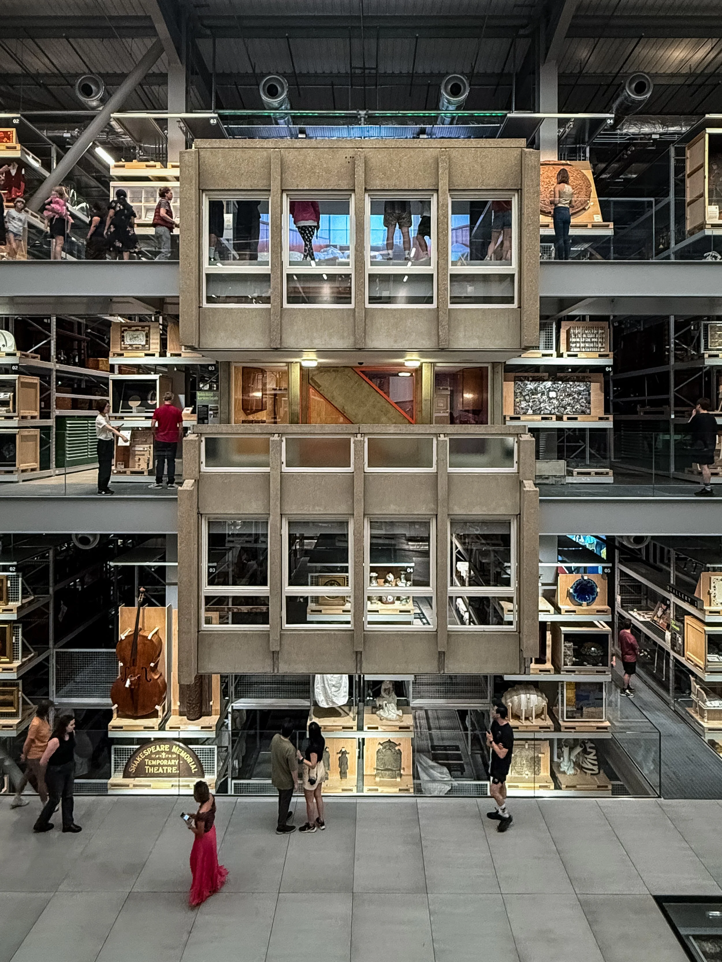 Interior of the V&A East Storehouse museum in London, United Kingdom. Multiple people walking and standing on different floors of a with art and display cases visible. Architecture photography. 