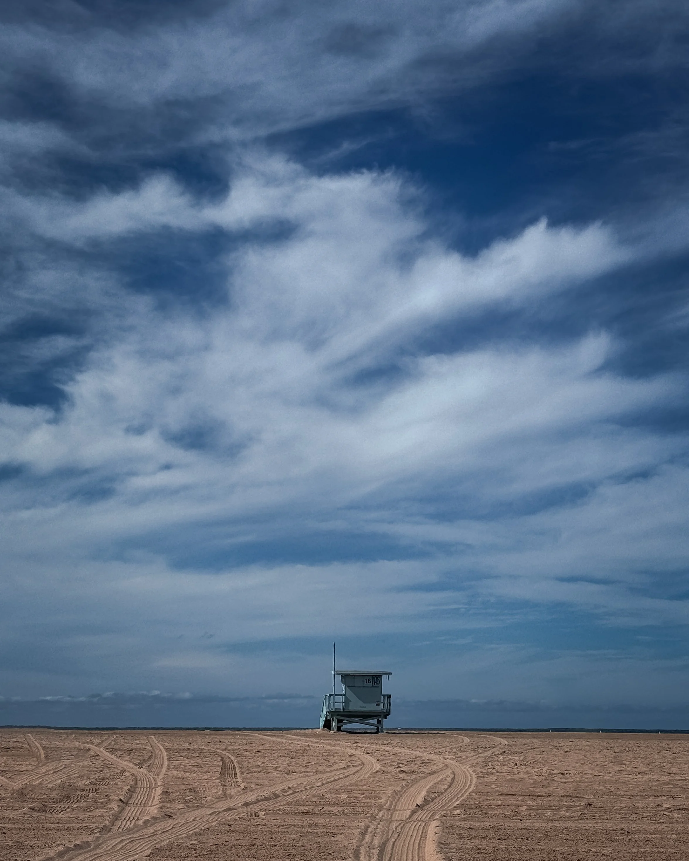 A lifeguard station on a sandy beach under a cloudy sky with blue and gray clouds.
