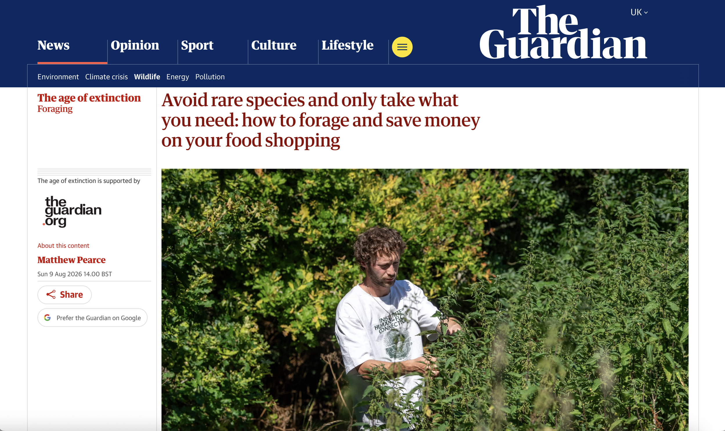 A man standing among green plants and trees, wearing a white t-shirt with text on it, in a lush outdoor setting.