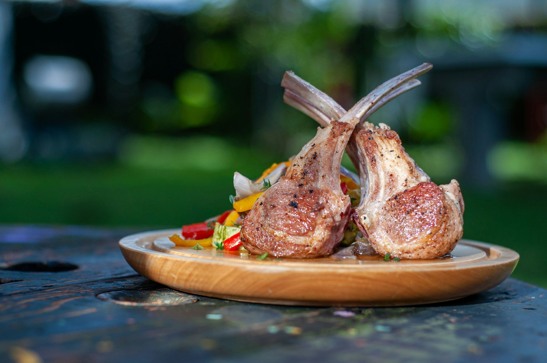 Grilled lamb chops with colorful vegetables on a wooden serving plate