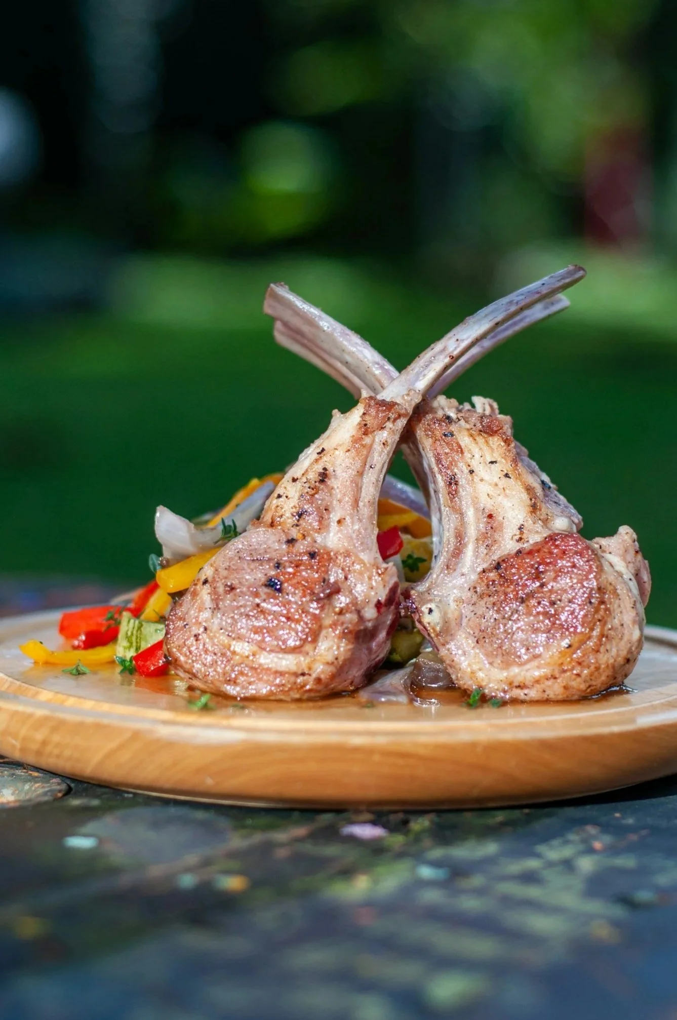 Grilled lamb chops with long bones served over colorful vegetables on a wooden platter