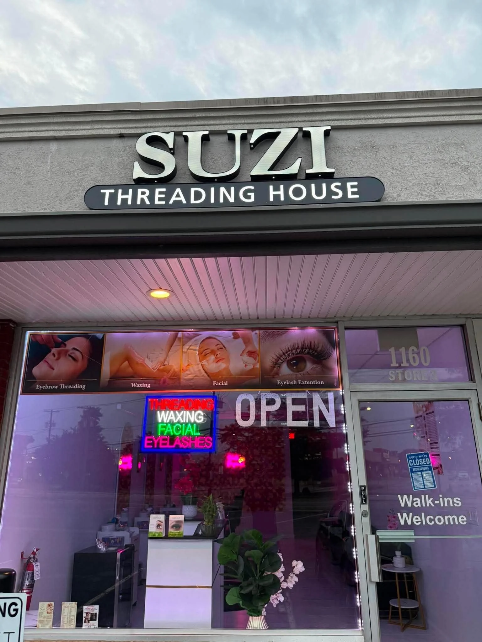Storefront for a beauty salon called 'Suz Threading House' with signage indicating services like eyebrow threading, waxing, facial, and eyelash extension. Neon signs in the window display services. The store is closed, and the entrance has a 'Walk-in