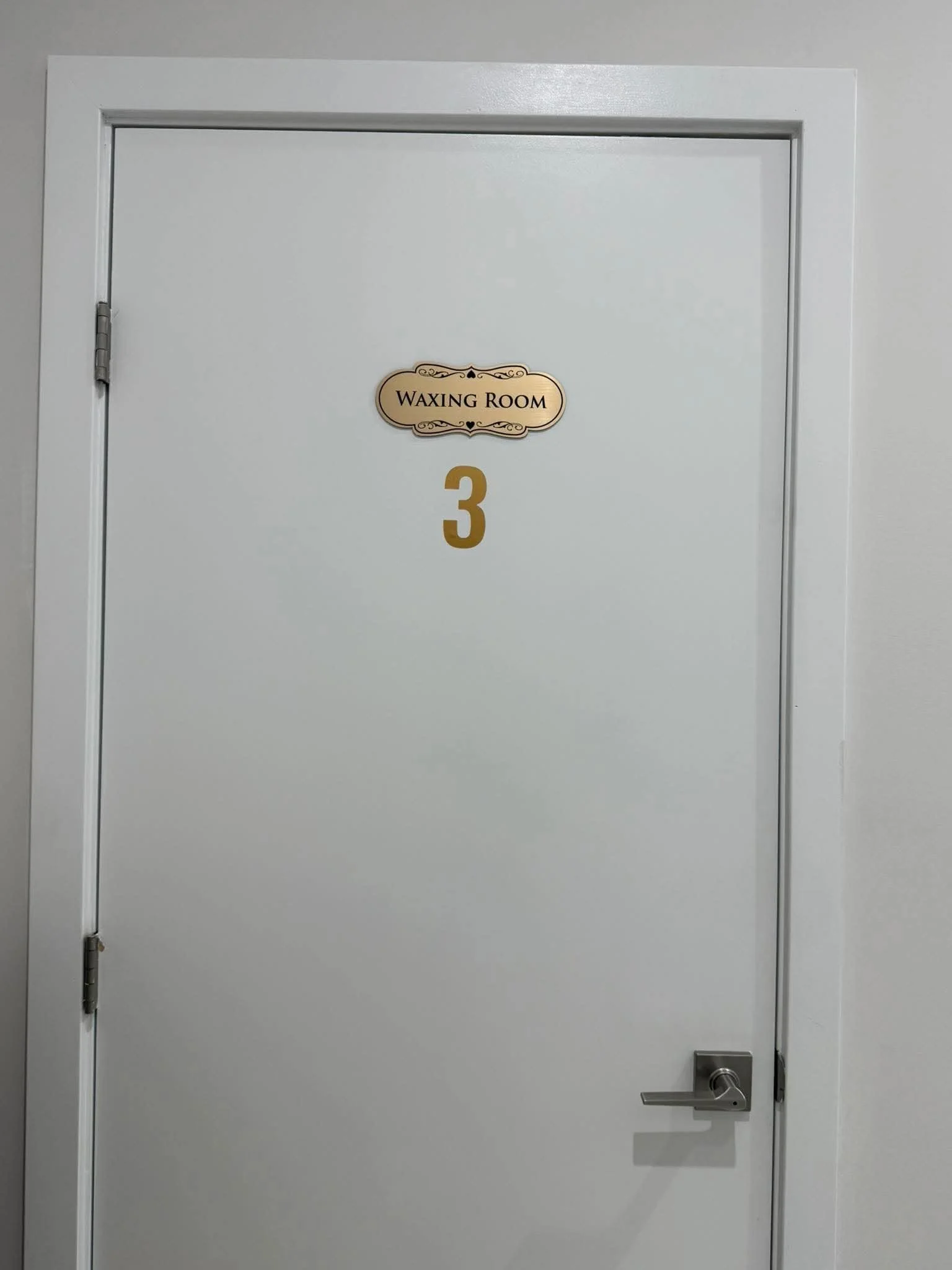 White door with a sign that reads 'Waxing Room' and the number 3 below it, with a silver door handle.
