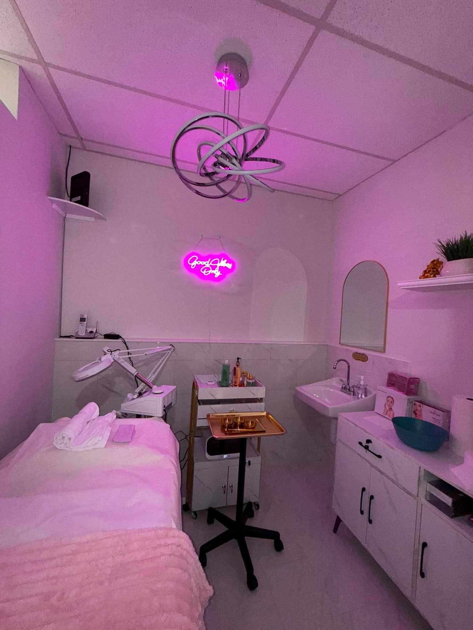 A nurse's or doctor's examination room with a pink bed, medical equipment, and a pink neon sign saying 'Good Vibes Only'