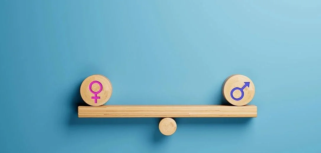 Une balance en bois avec deux cercles en bois portant des symboles féminins et masculins, sur un mur bleu.