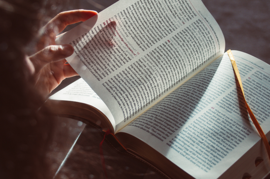 Une main tient une page d'un livre ouvert, avec un rayon de lumière passant à travers la page, créant une ombre sur le texte en dessous.