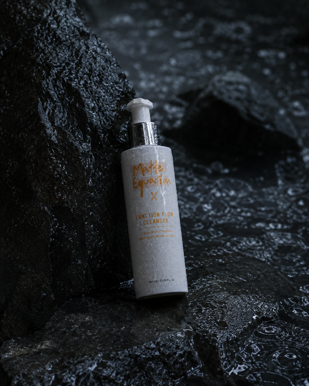 A white bottle of Matte Equity Function Flow Cleanser with orange text, lying on wet dark rocks near flowing water.