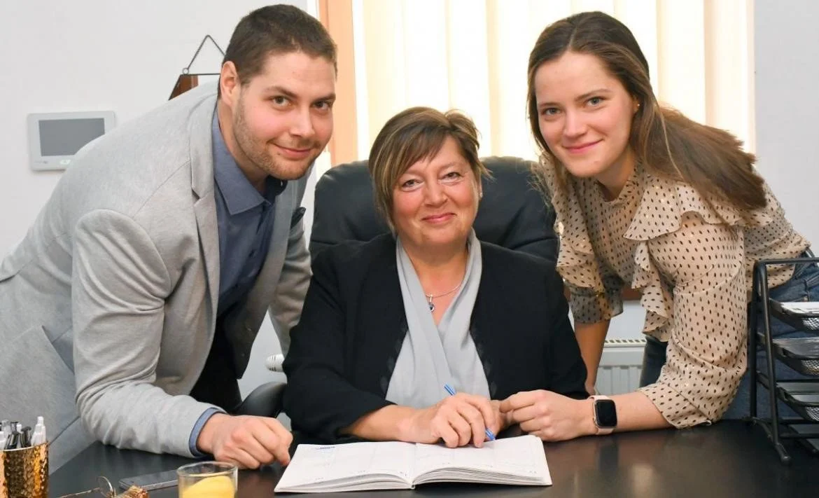 Three people, two women and one man, posing together in an office around a desk with an open notebook.