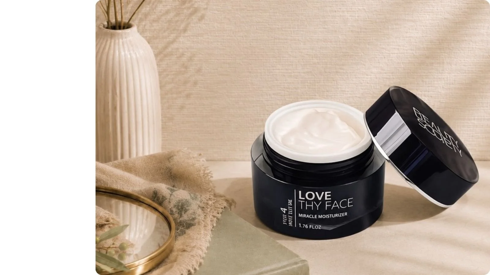 Beauty Society Love Thy Face Miracle Moisturizer in a black jar with the lid removed, showing the rich moisturizing cream inside.