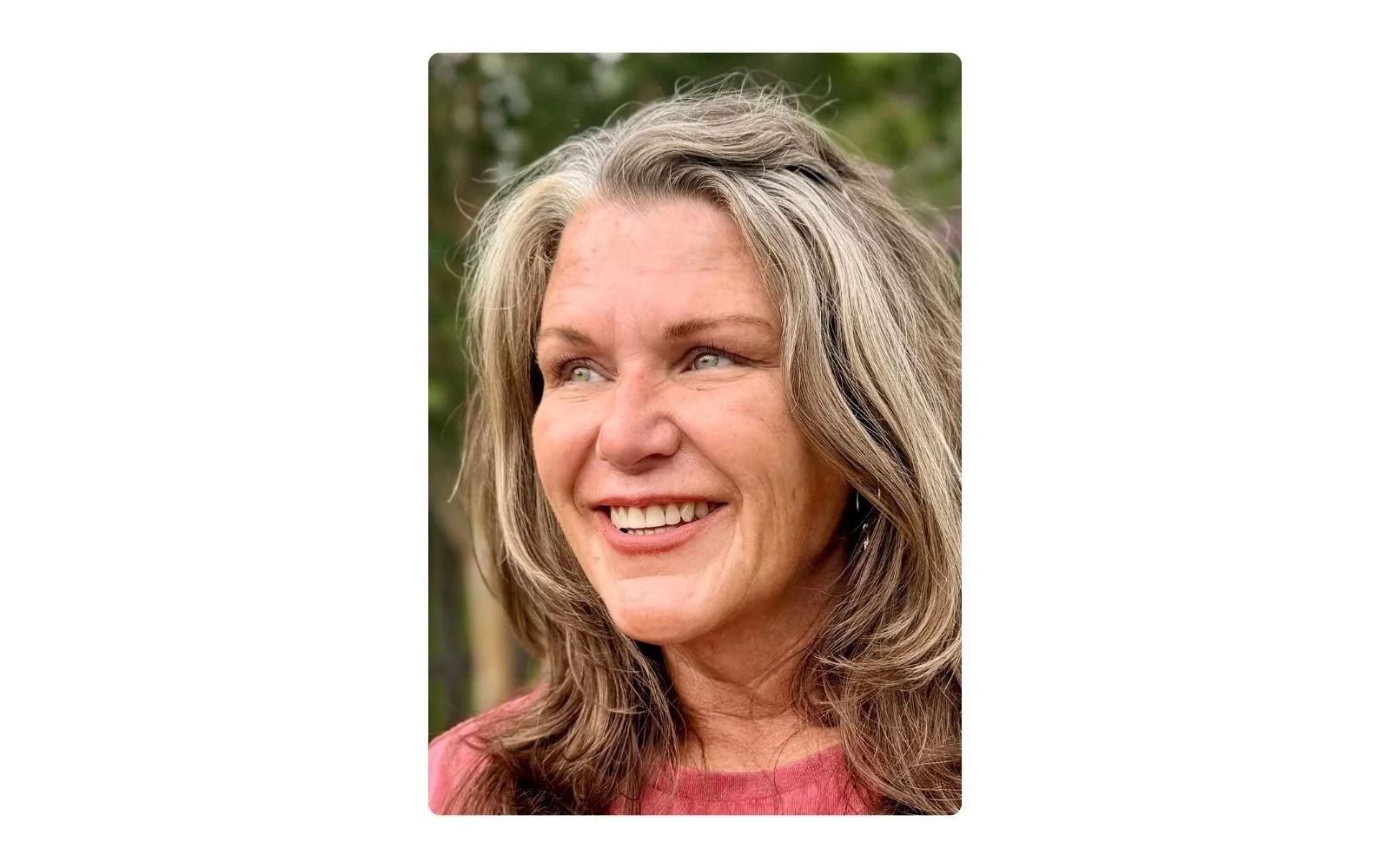 Close-up portrait of Julie outdoors with fresh, moisturized skin, natural silver-streaked hair, and a relaxed smile in soft natural light.
