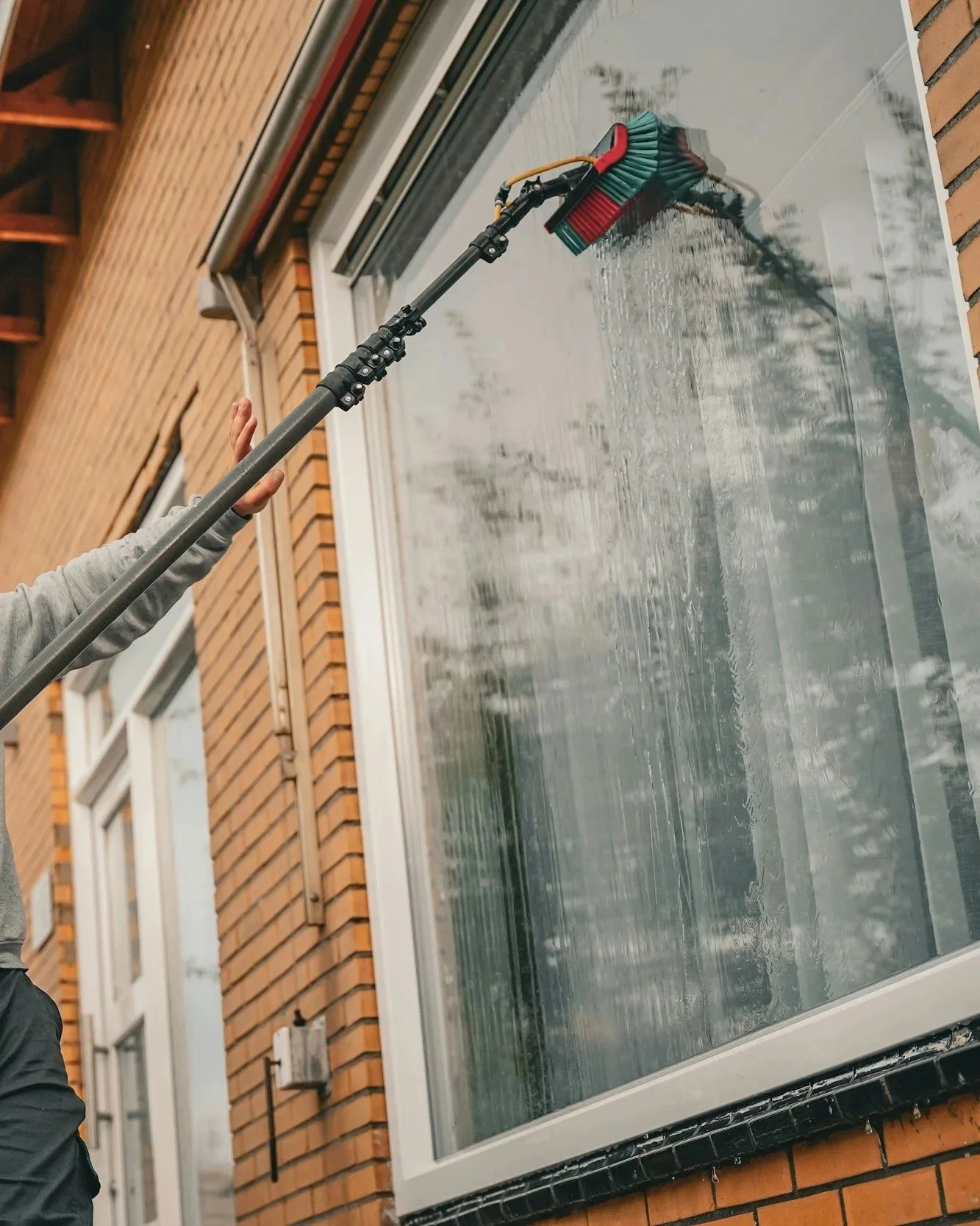 Person cleaning a large window on a brick building using a water fed pole system.