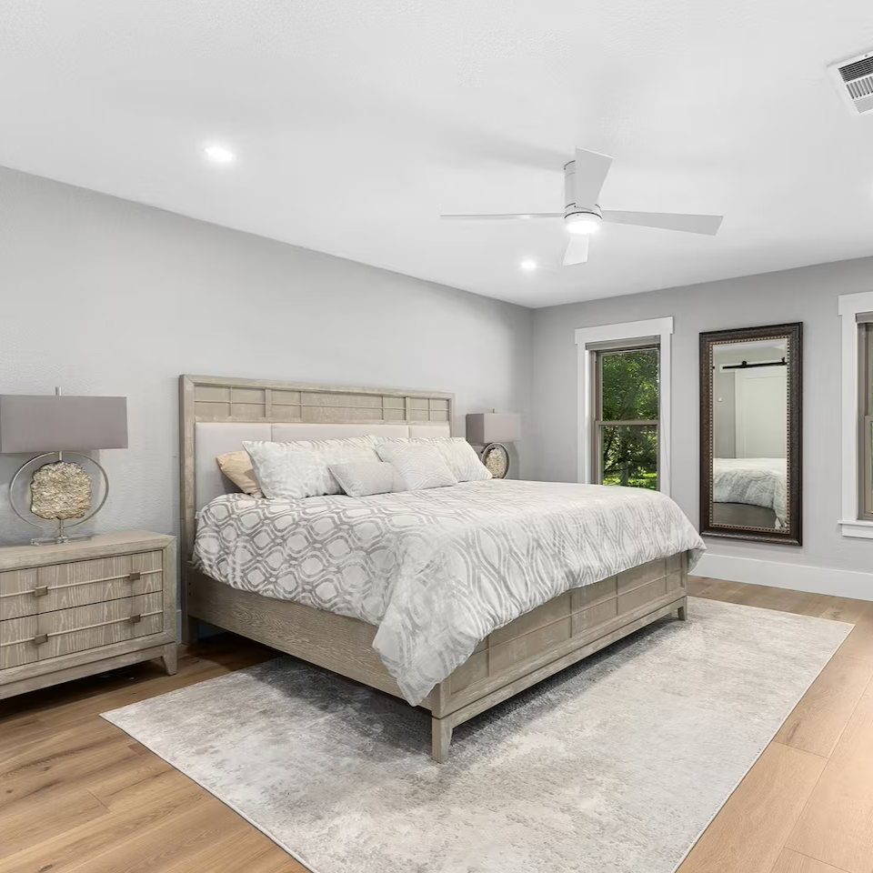 Bedroom with a king-size bed, wooden nightstand, mirror, and windows.