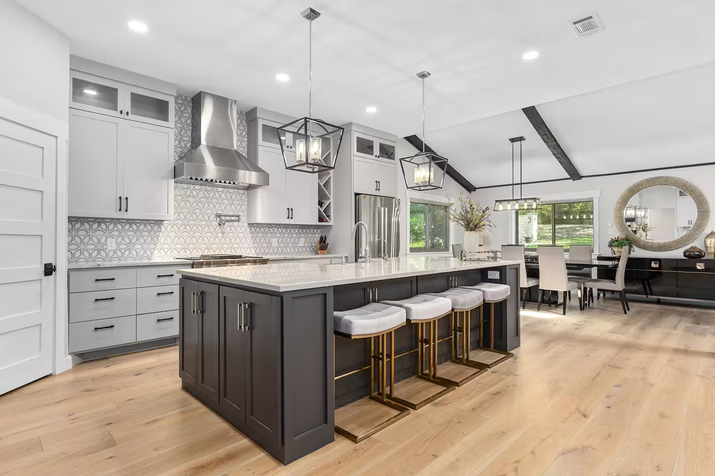 Modern open-concept kitchen and dining area with white cabinetry, a dark gray island, and light wooden flooring.