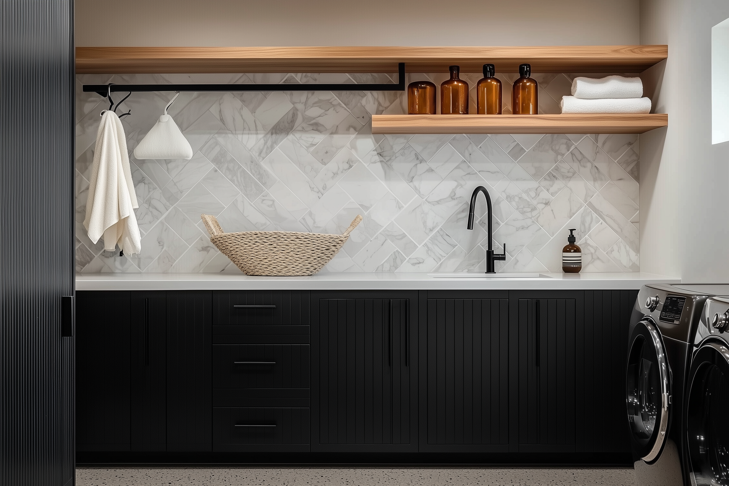 A modern laundry room with black cabinetry, marble herringbone backsplash, wooden shelves, amber glass jars, and a matte black faucet, exuding luxury and elegance.