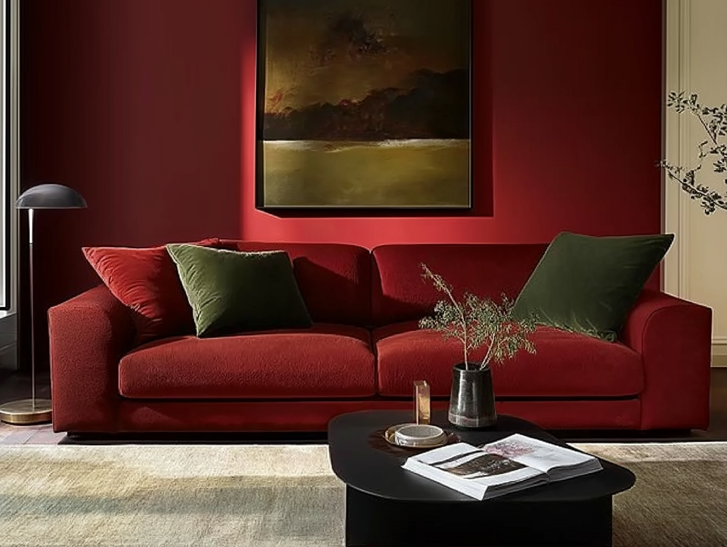 Living room with Farrow & Ball Rectory Red walls, a crimson sofa, green velvet throw pillows, a black coffee table, and moody landscape artwork for a dramatic yet cozy ambiance.