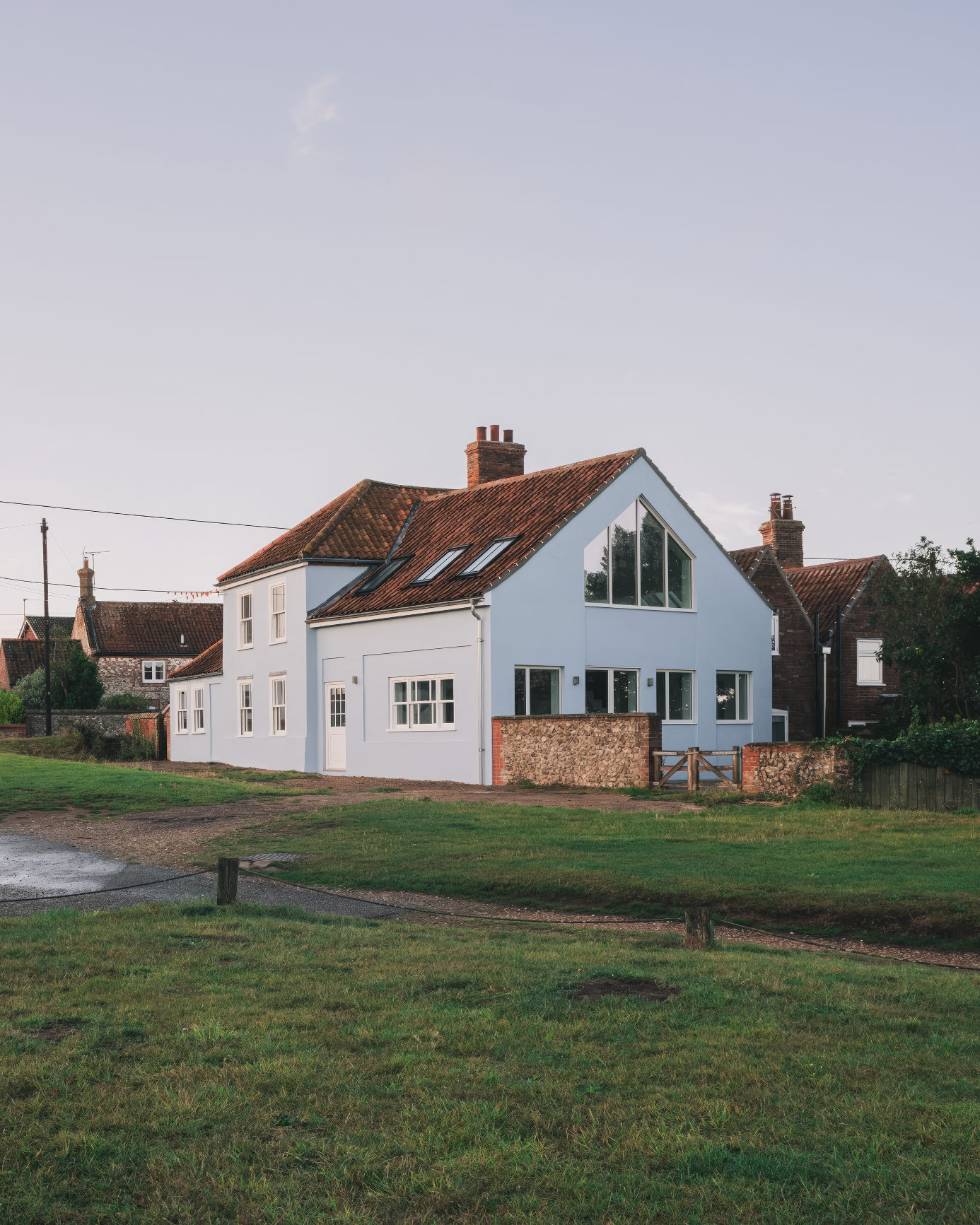 Blue-painted coastal home with clay roof tiles, large gable window, and traditional cottage features surrounded by green grass.