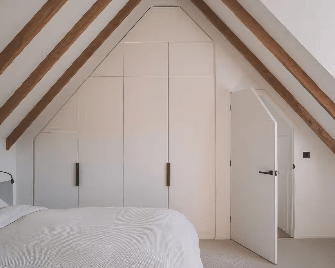 Vaulted bedroom with exposed wooden beams and custom-built wardrobes fitted into the sloped ceiling, with matte black handles.