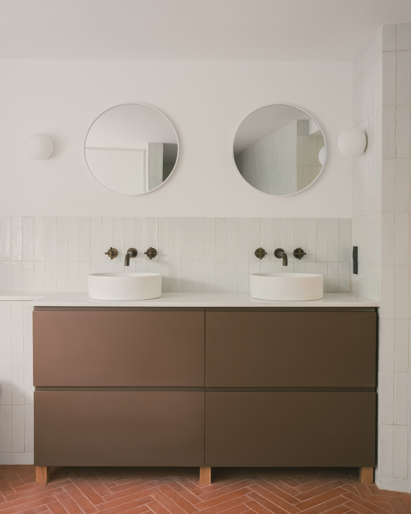 Double vanity with round mirrors and rich brown cabinetry.