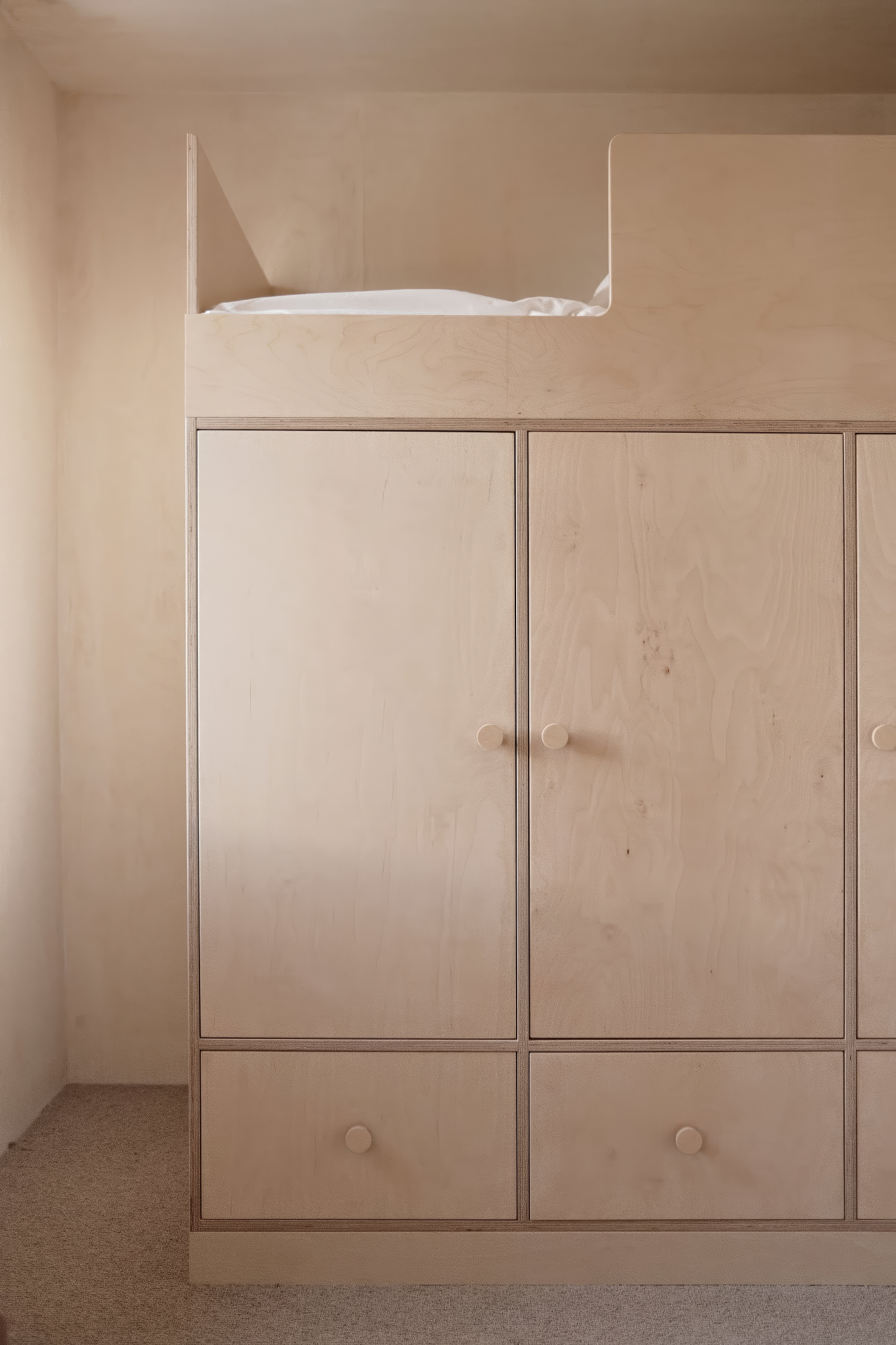 Scandinavian-inspired wooden bunk bed unit with integrated wardrobe and drawers, crafted in light plywood with rounded knobs, set against a neutral-toned wall.