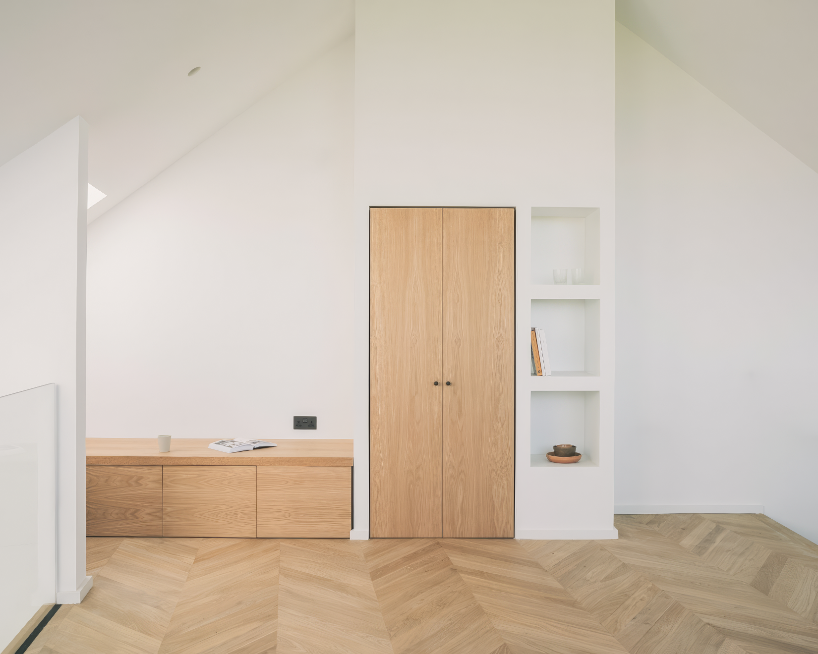 Minimal hallway featuring pale chevron wood flooring, integrated oak cabinetry, and open shelving built into white walls.