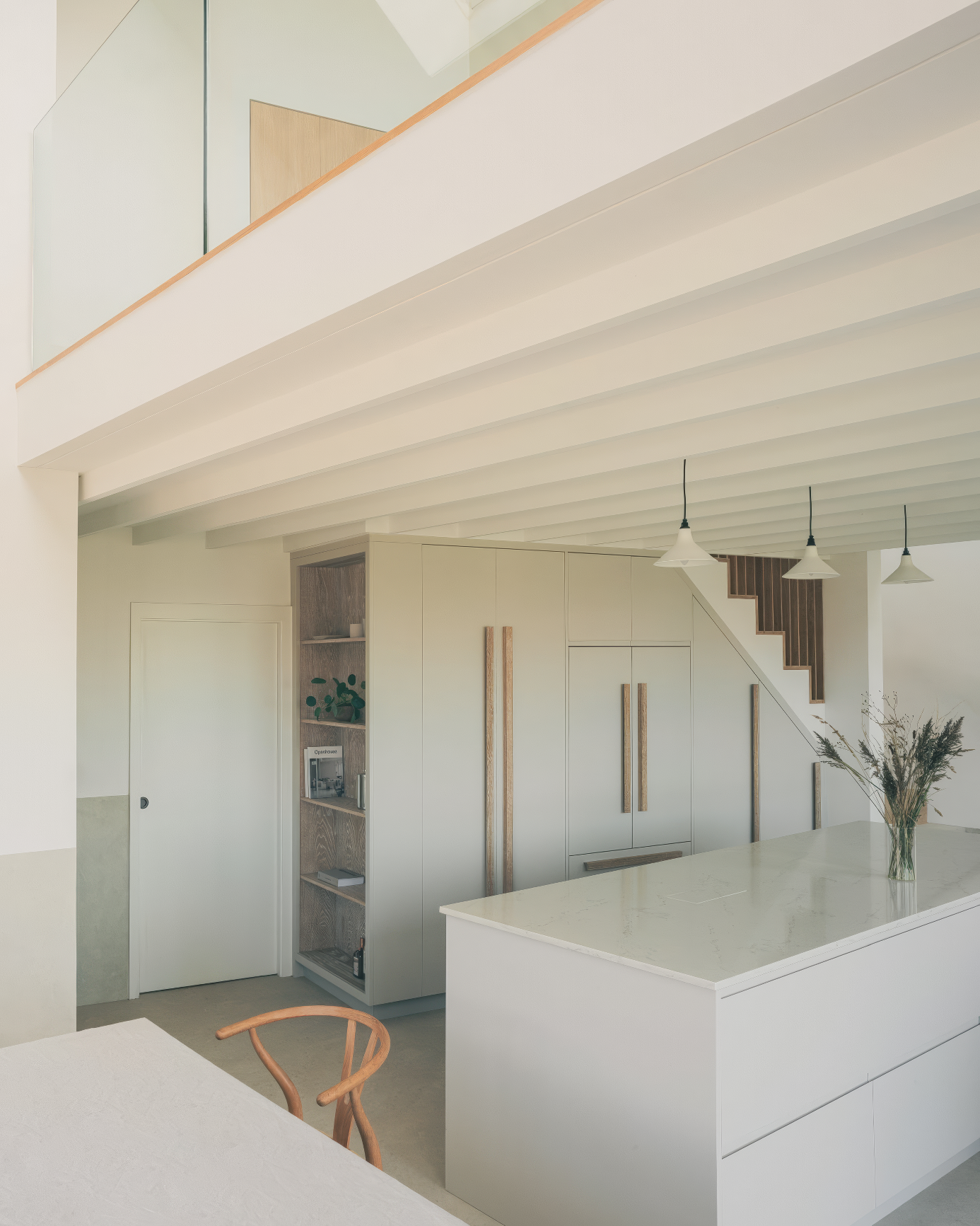 Open-plan kitchen with tall cabinetry, island, and glass stair balustrade.
